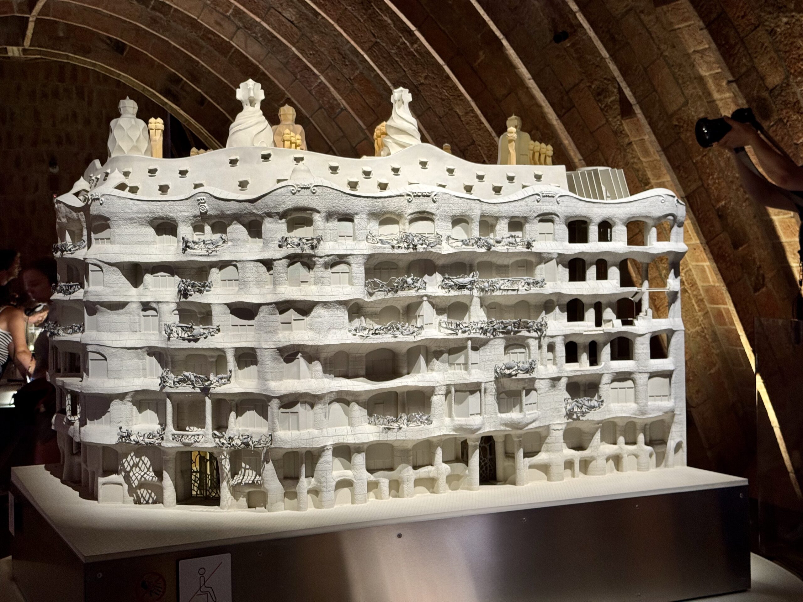 White, multi-story architectural model with wavy façades and numerous balconies displayed indoors under a brick arch ceiling.