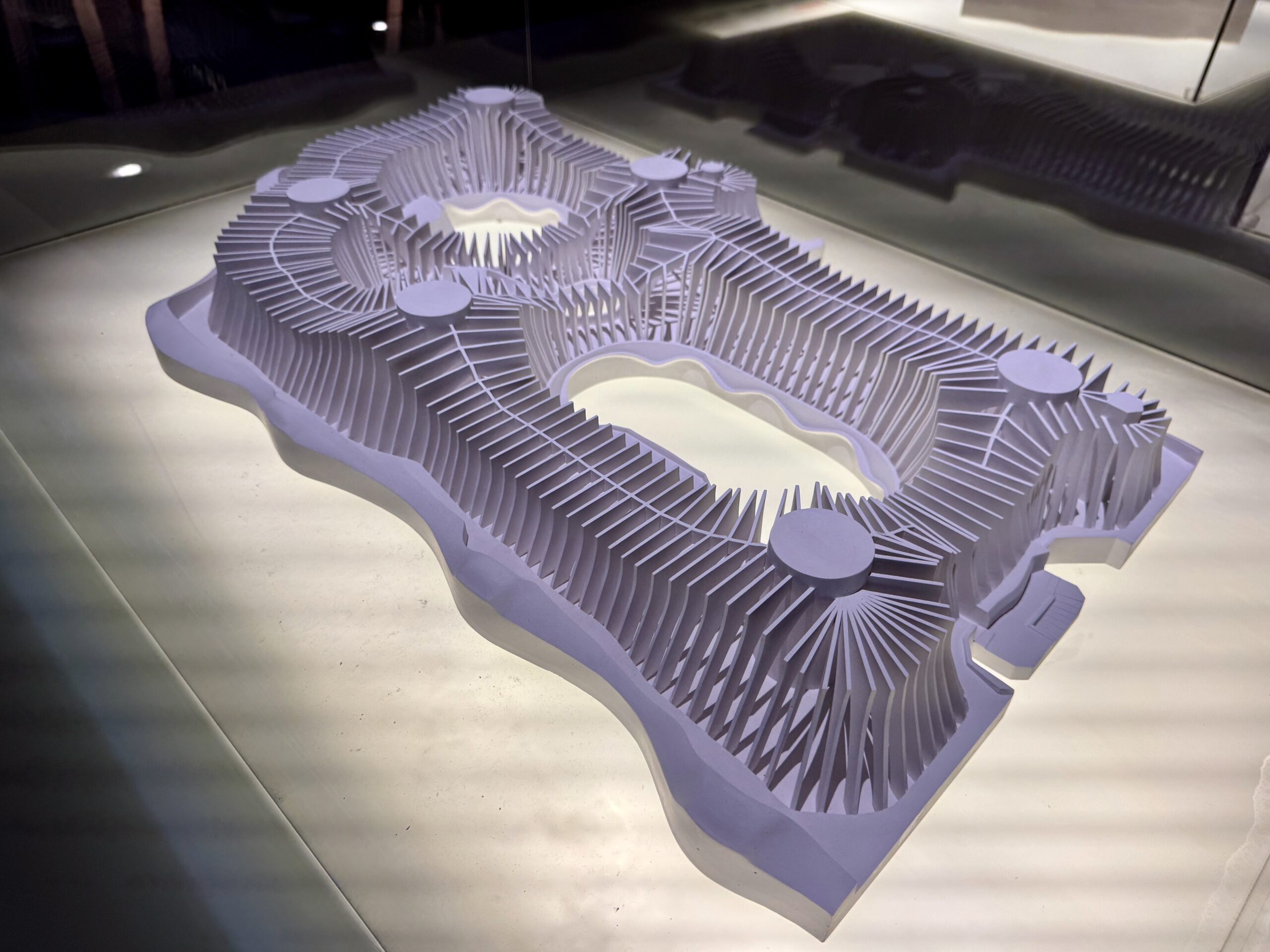 Abstract sculpture made of stacked vertical fins forming ridged hills with circular platforms on a reflective surface.
