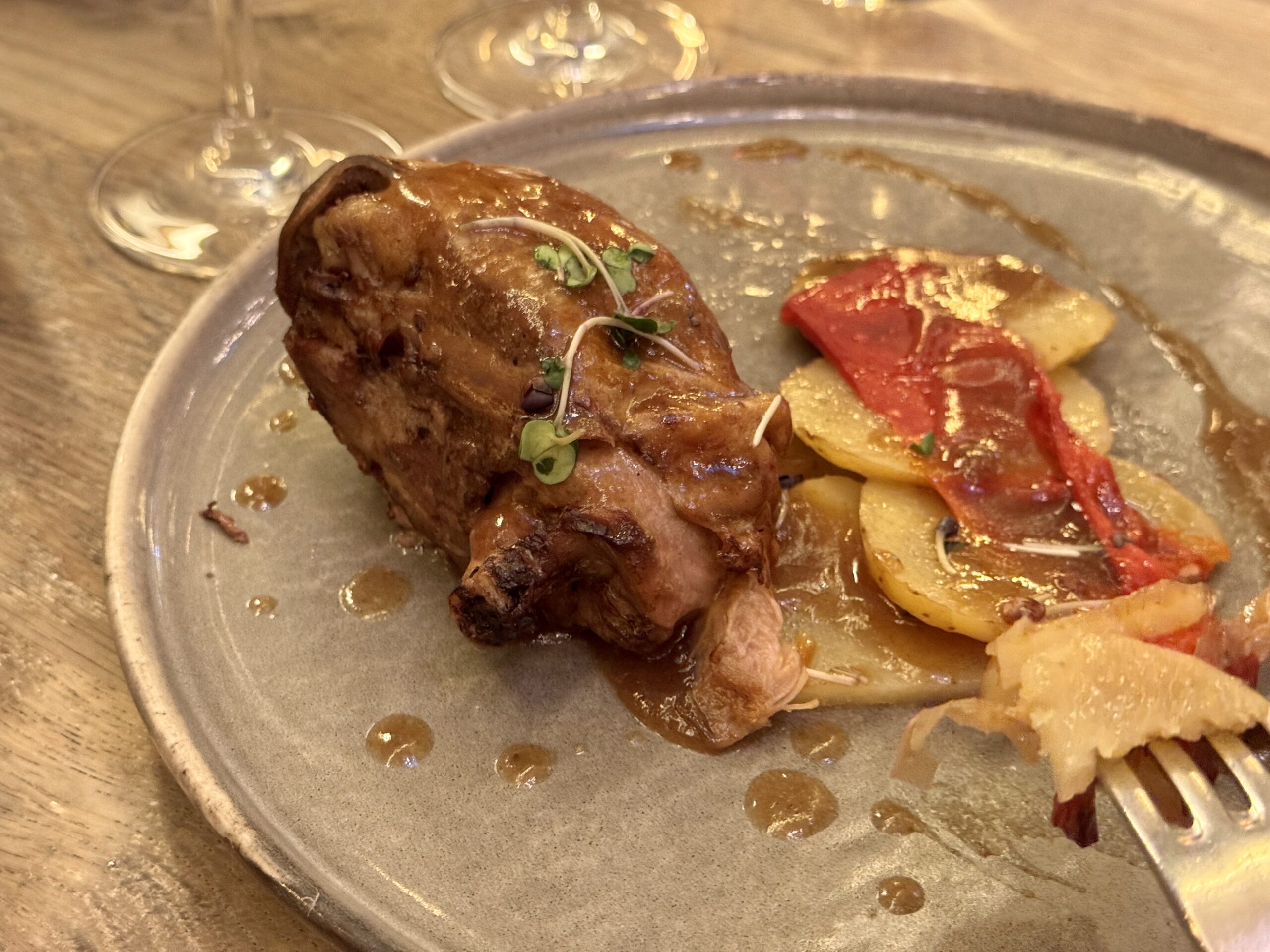 Roasted meat with herbs on a plate, next to roasted potatoes and red peppers, with glossy sauce droplets on a gray plate.