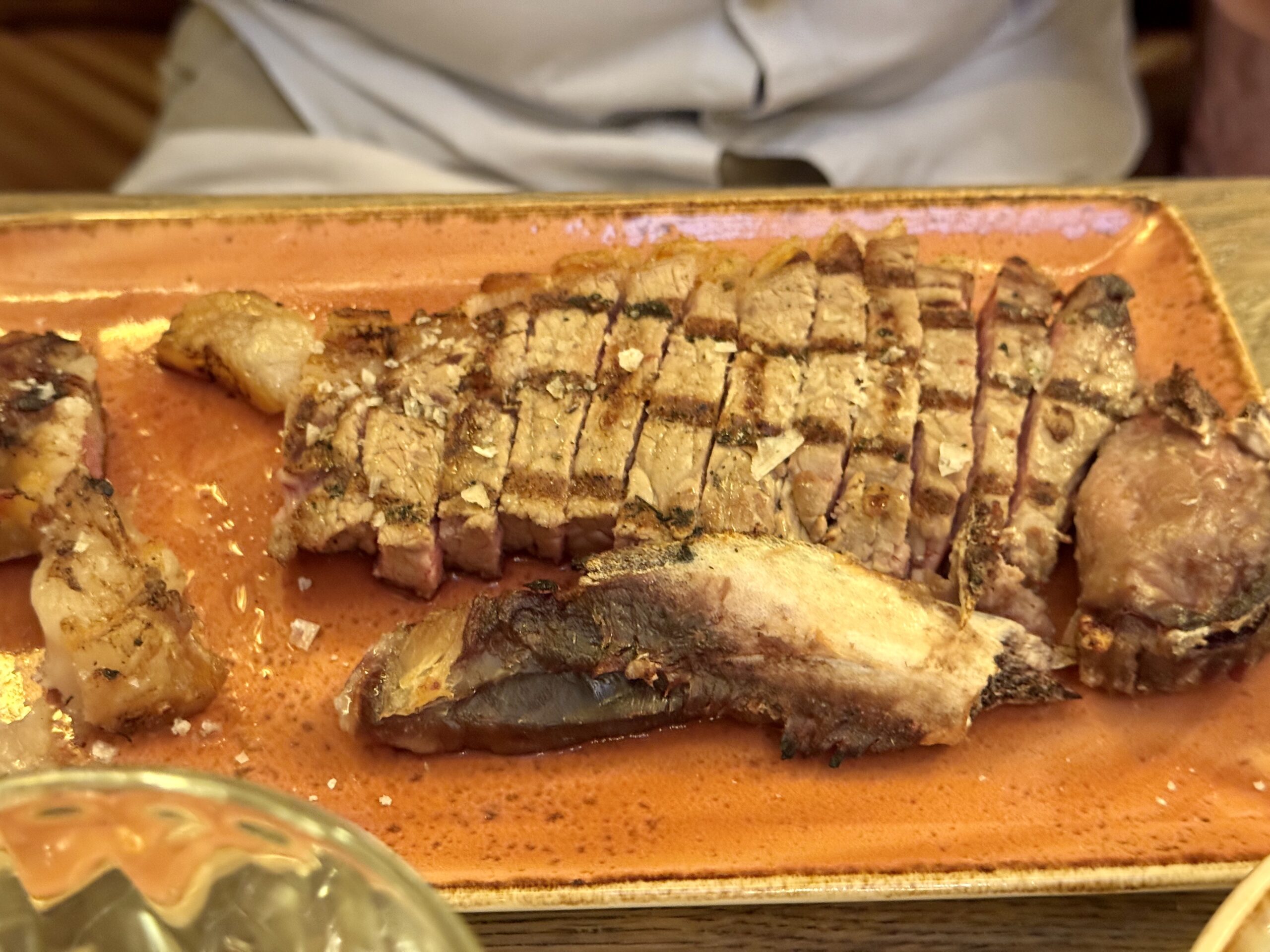 Sliced beef roast with a crumbly herb crust on an orange baking sheet, juices pooling around the meat amid a kitchen scene