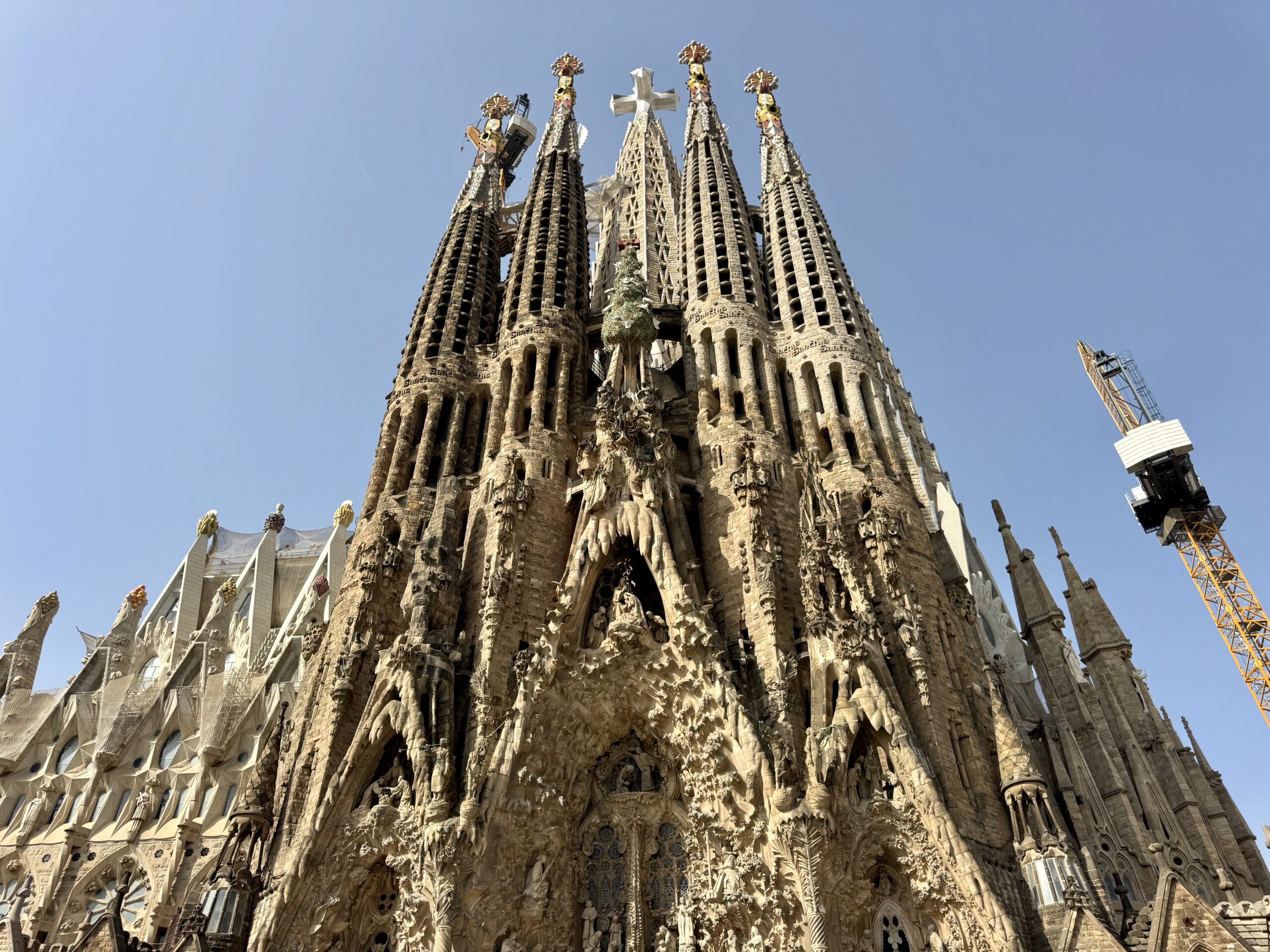 Facade of Sagrada Família with tall spires and intricate stone carvings against a clear blue sky