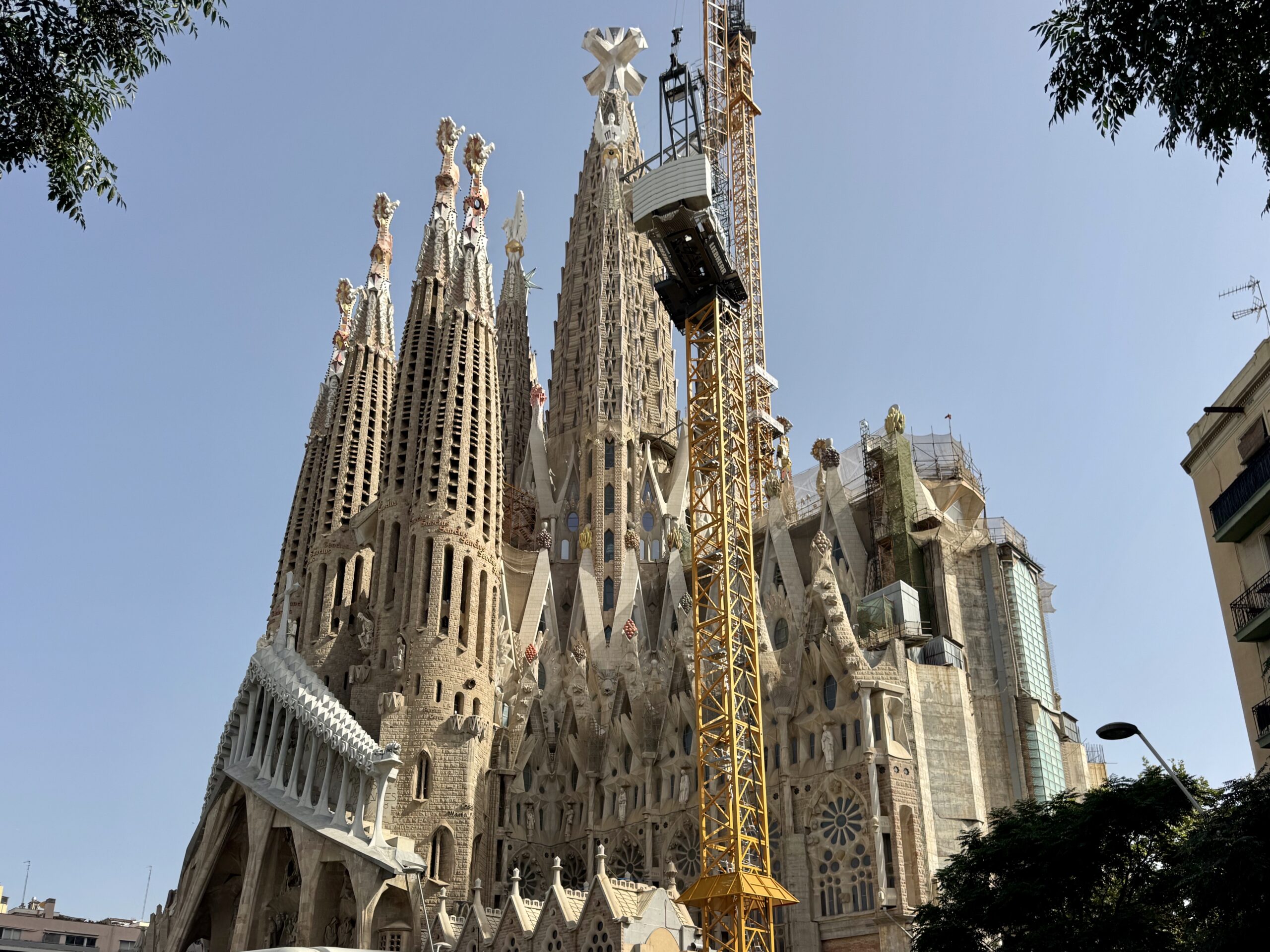 Sagrada Família cathedral in Barcelona with tall spires and a yellow construction crane against a blue sky.