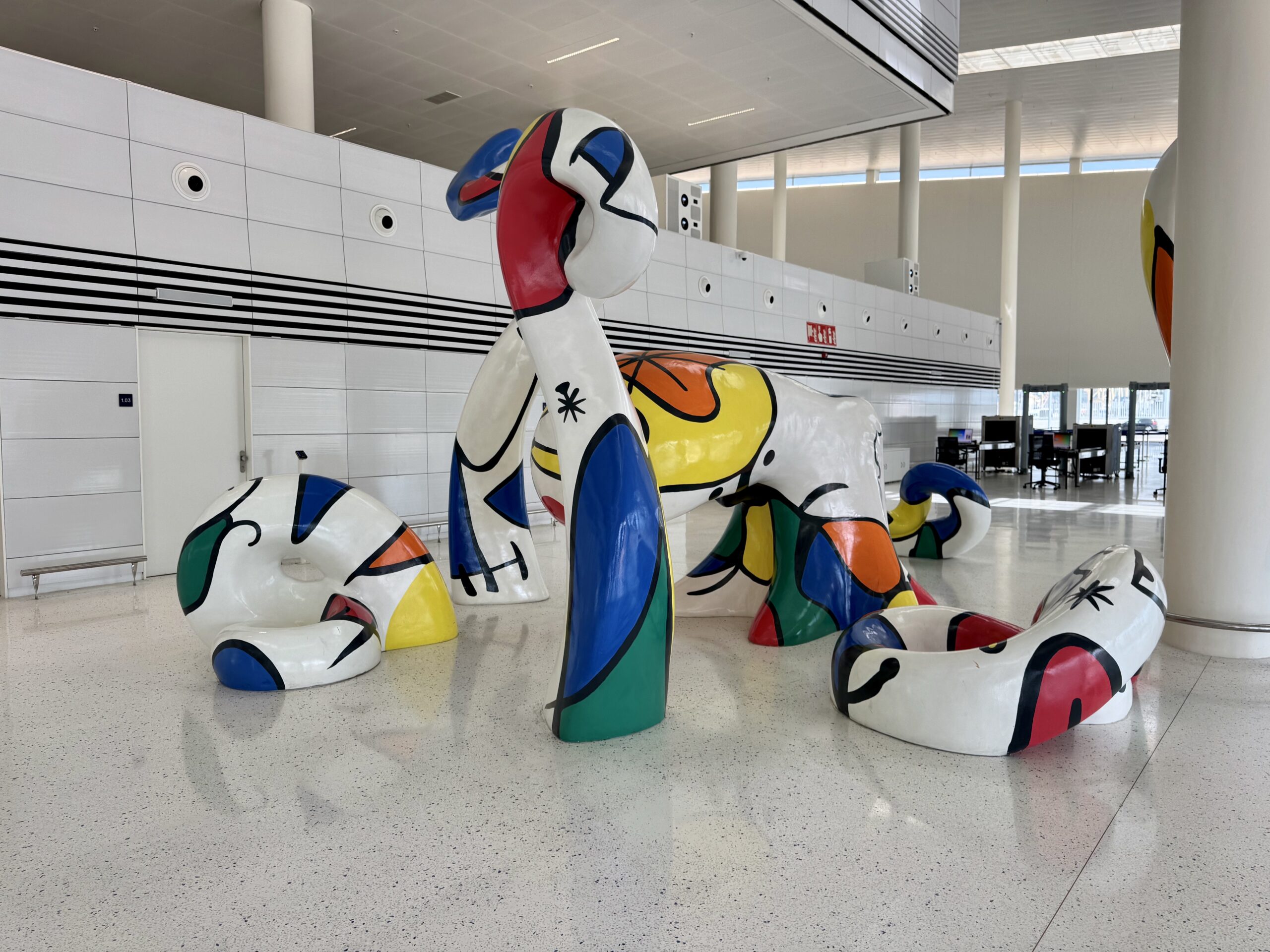 Large abstract elephant sculptures painted in bright colors stand in a bright, modern atrium with white tiled walls and high ceilings.