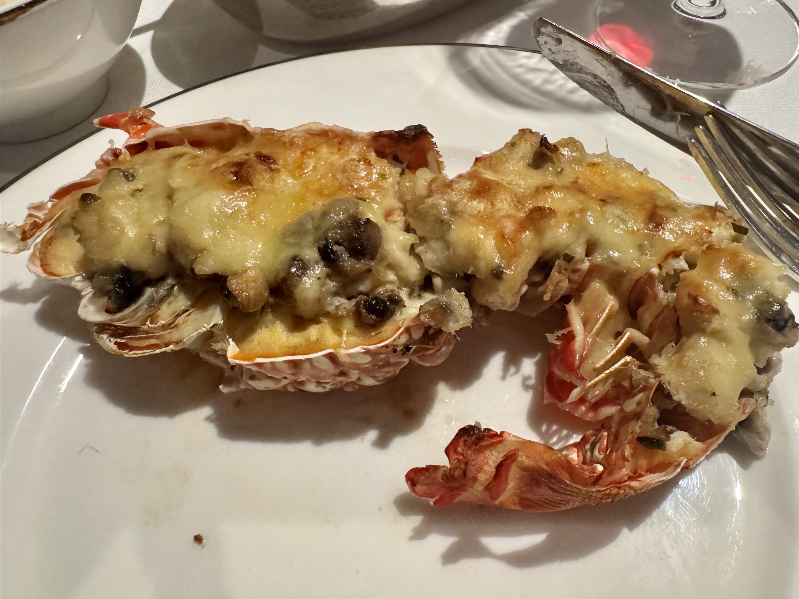 Two lobster tail halves topped with melted cheese on a white plate.
