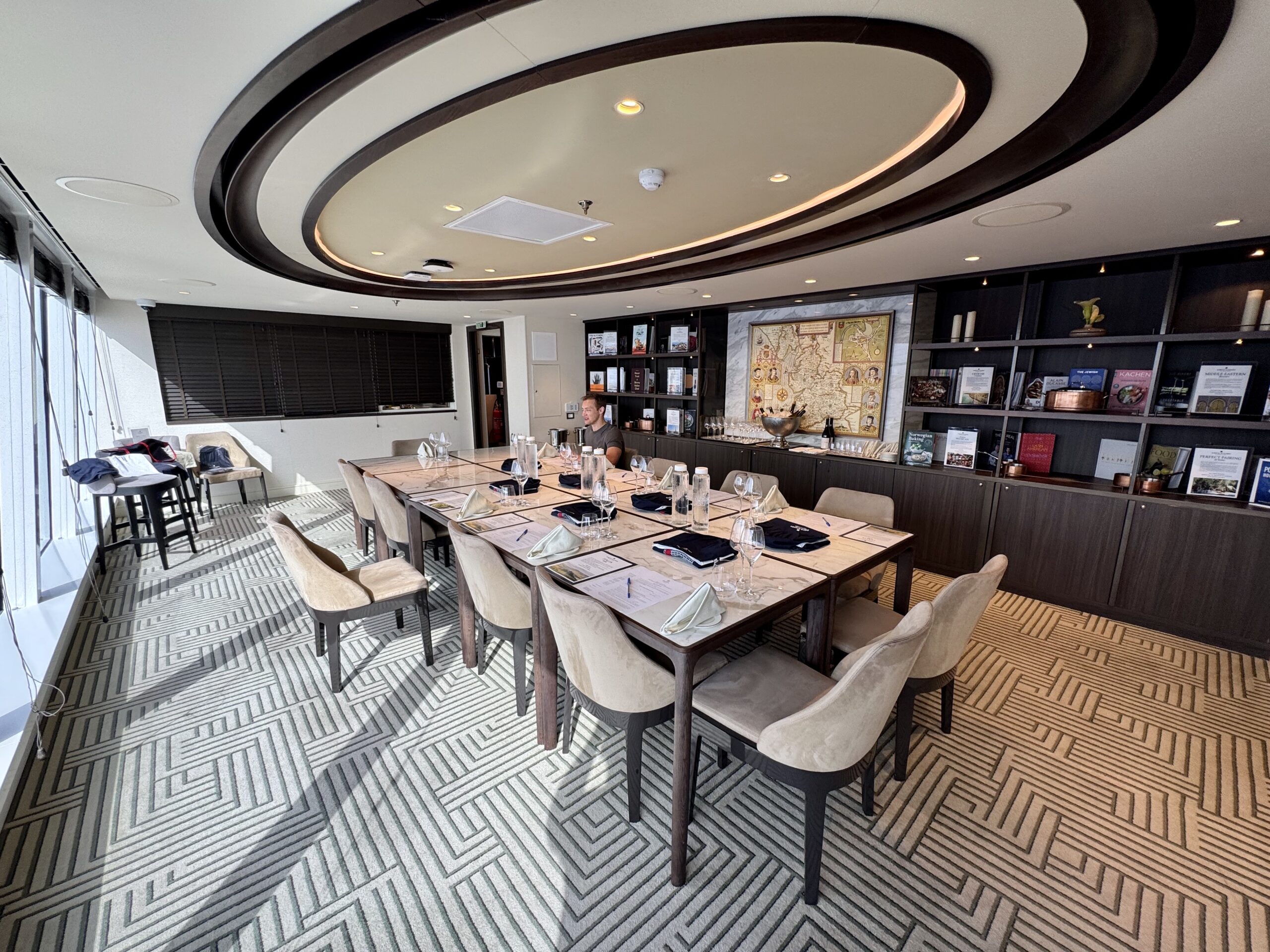 Meeting room with a long table set for lunch, beige chairs, and wall-to-wall bookshelves; circular ceiling design explains space use.