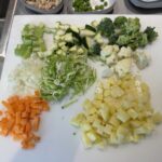 Assorted chopped vegetables on a cutting board: diced carrots, potatoes, zucchini, broccoli, cauliflower, and shredded cabbage.