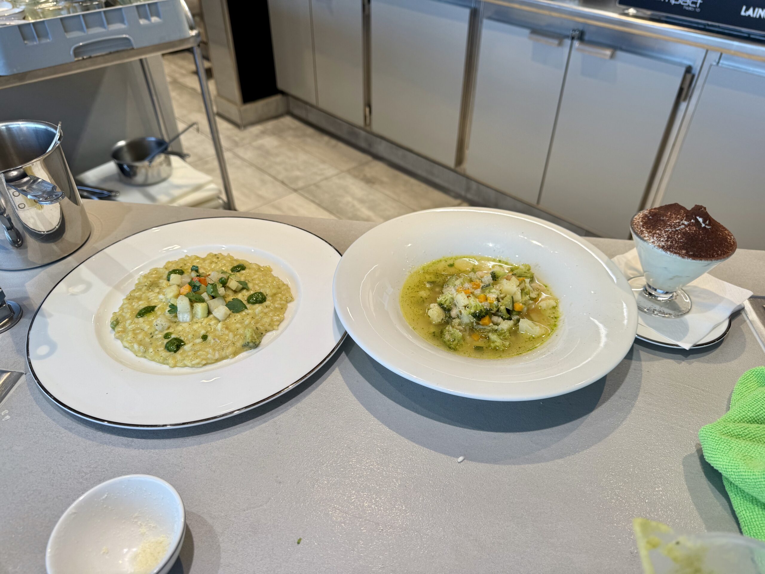 Two bowls of soup on a counter with a dessert glass on the right and a metal pitcher nearby in a kitchen setting.