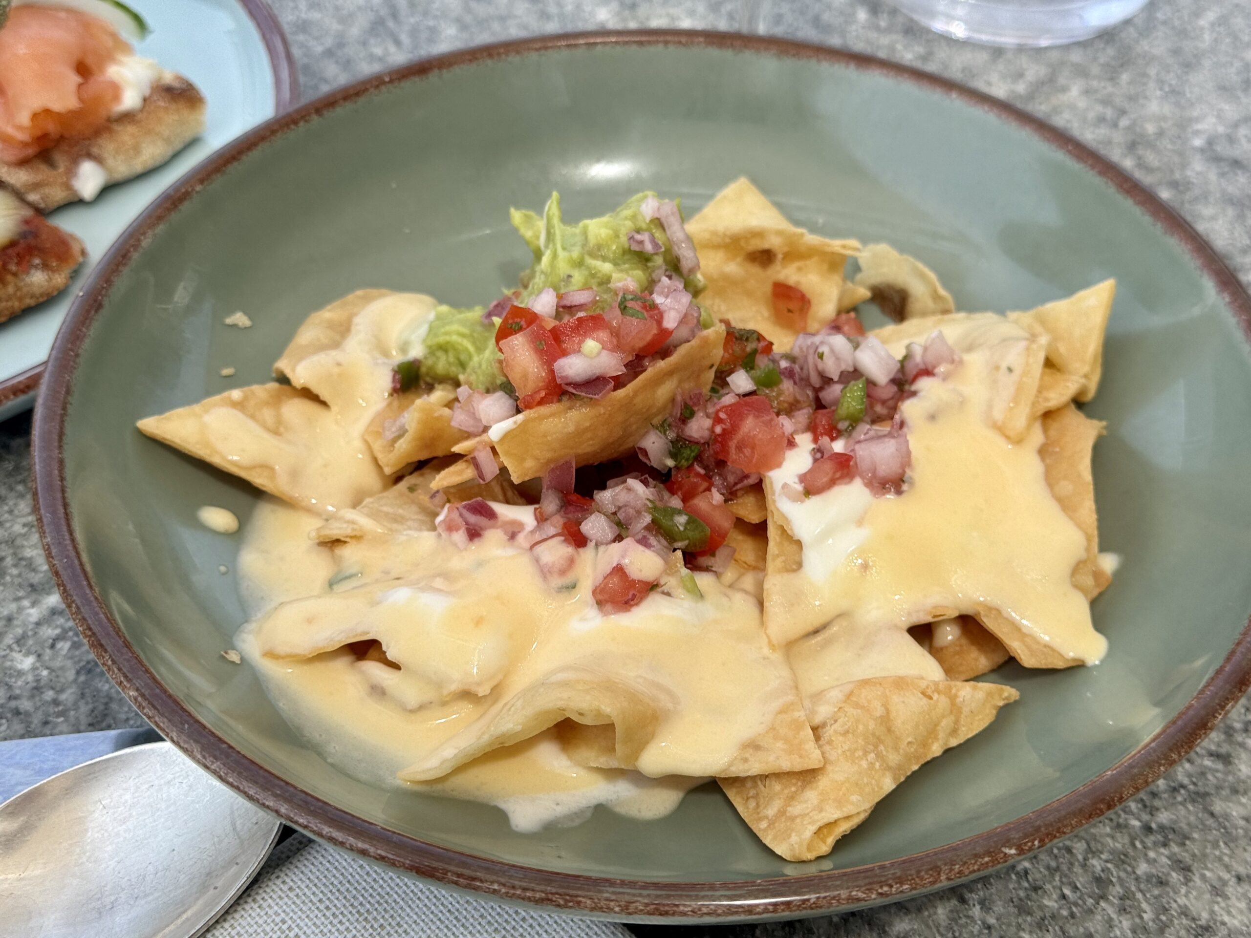 Bowl of tortilla chips with melted cheese and fresh pico de gallo topping, alongside guacamole.