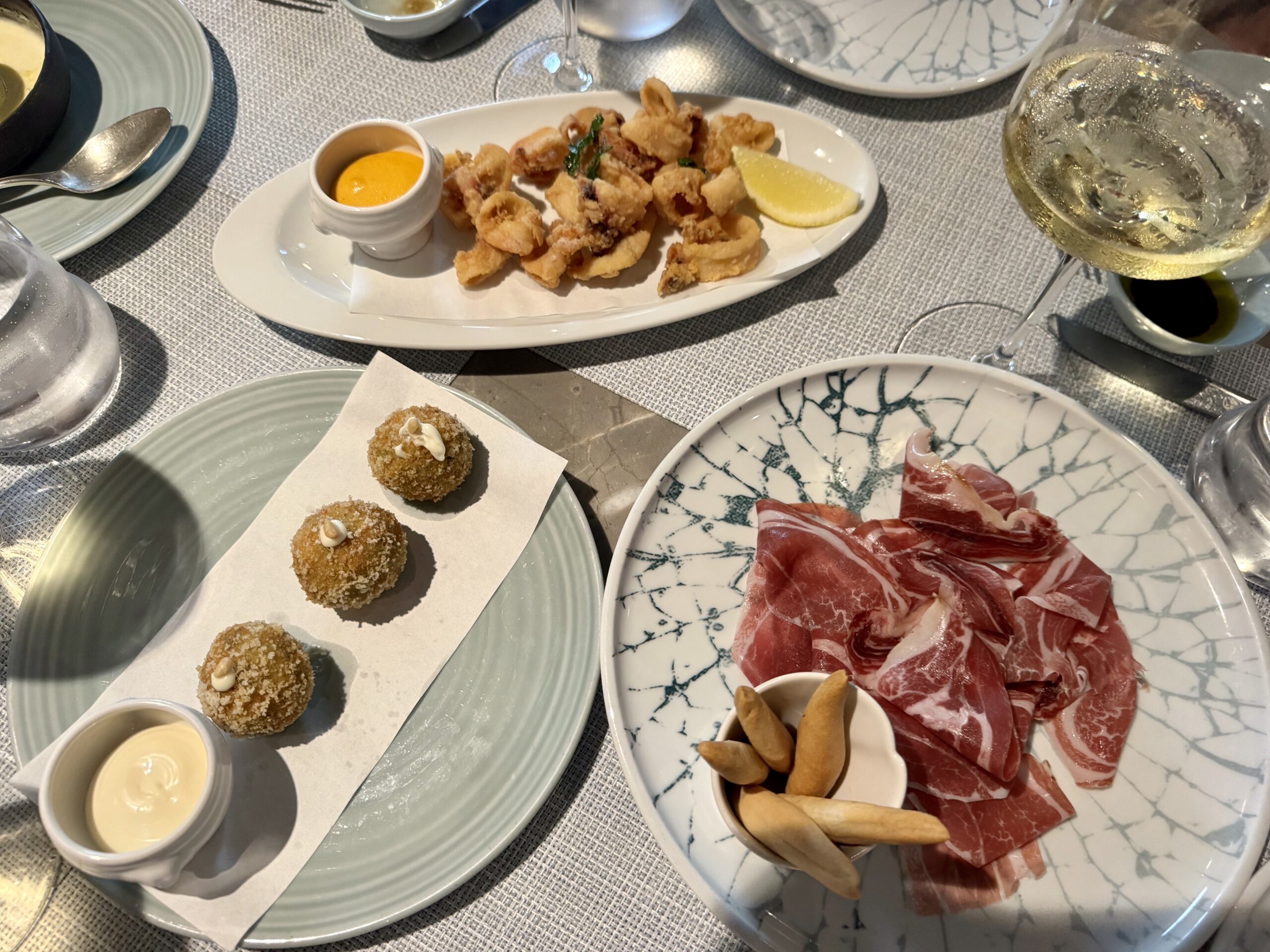 Plate of fried bite-sized calamari with lemon wedge and dipping sauces, set with other plates on a dining table.