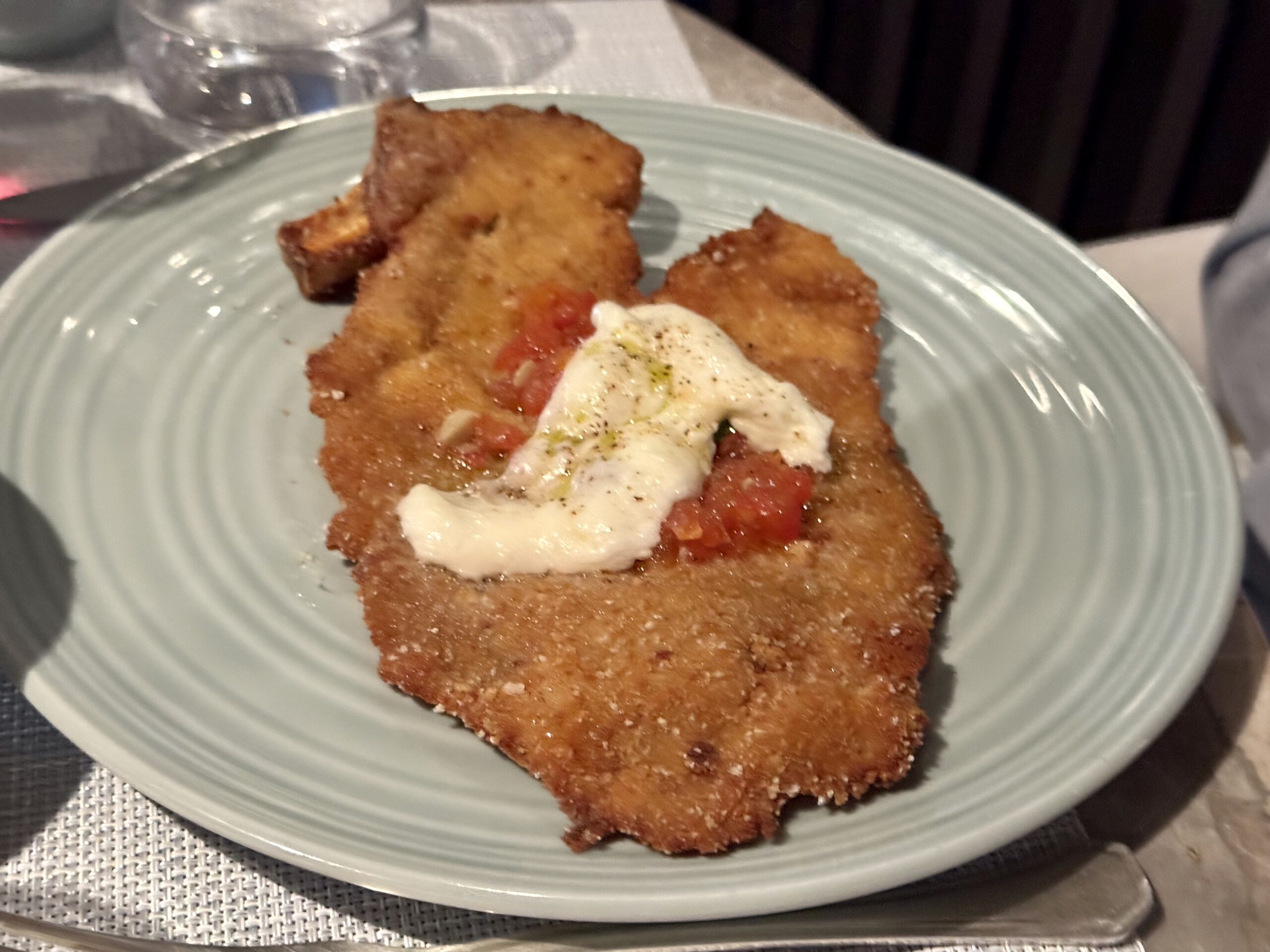 Two crispy breaded fried cutlets on a pale green plate topped with a dollop of sour cream and a sprinkle of herbs.