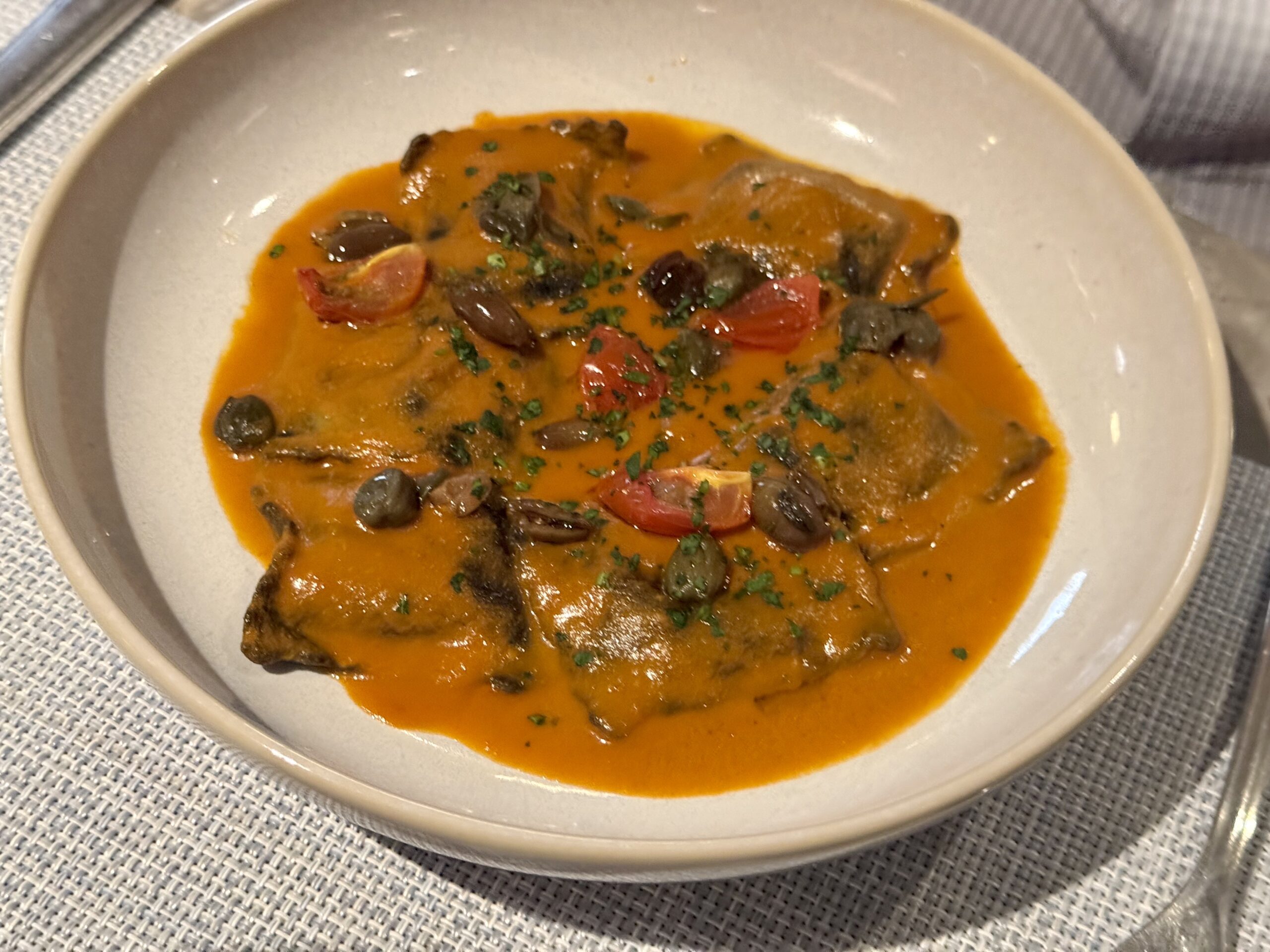 Chicken in a tomato-orange sauce with olives, mushrooms, and herbs served in a shallow bowl.