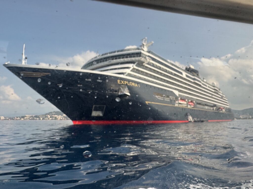 Large cruise ship in a harbor with 'EXPLORA' on the hull, viewed through a rain-speckled window.