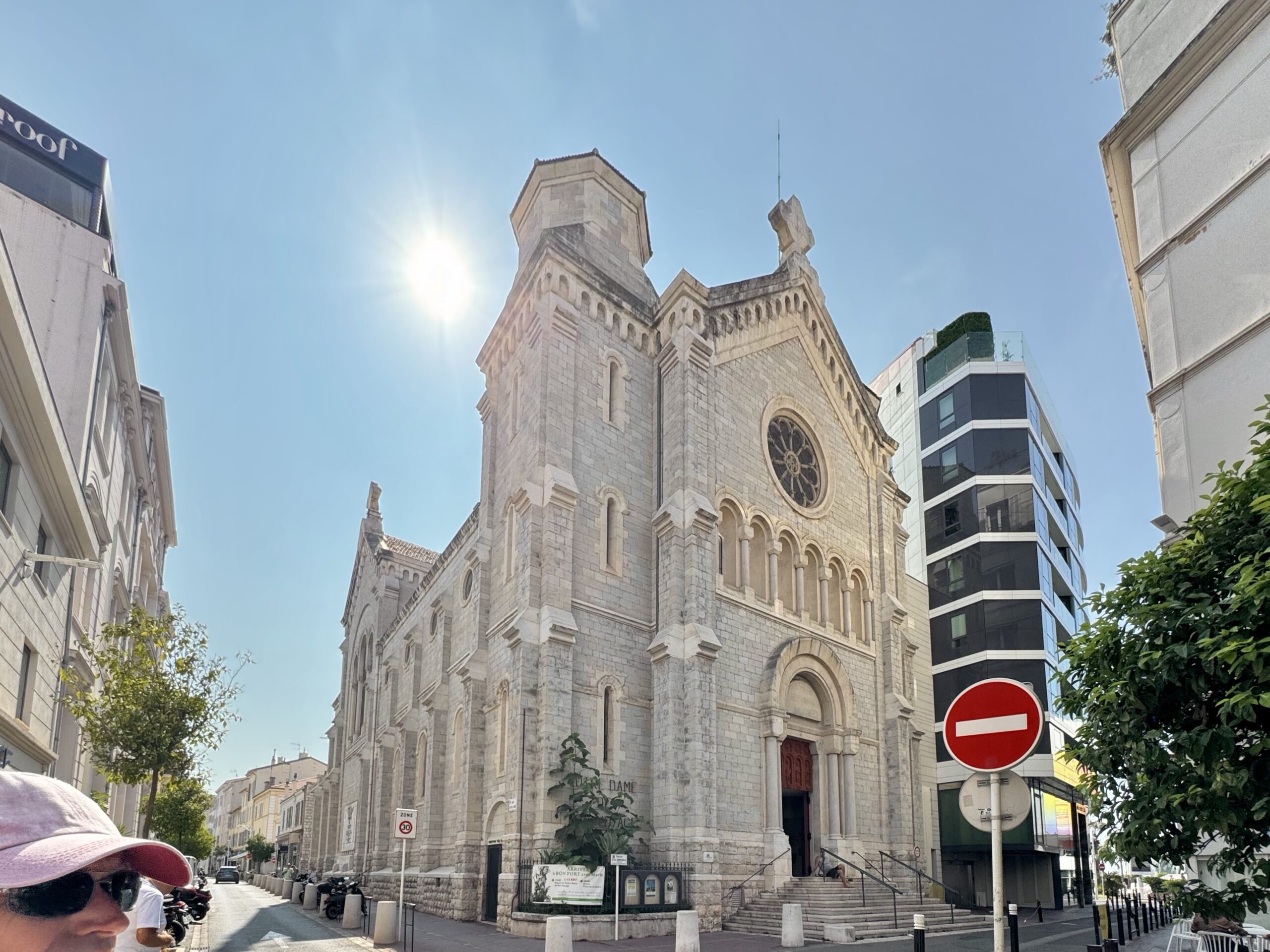 Historic stone church on a sunny city street, with a modern glass building to the right and a no-entry sign in the foreground.