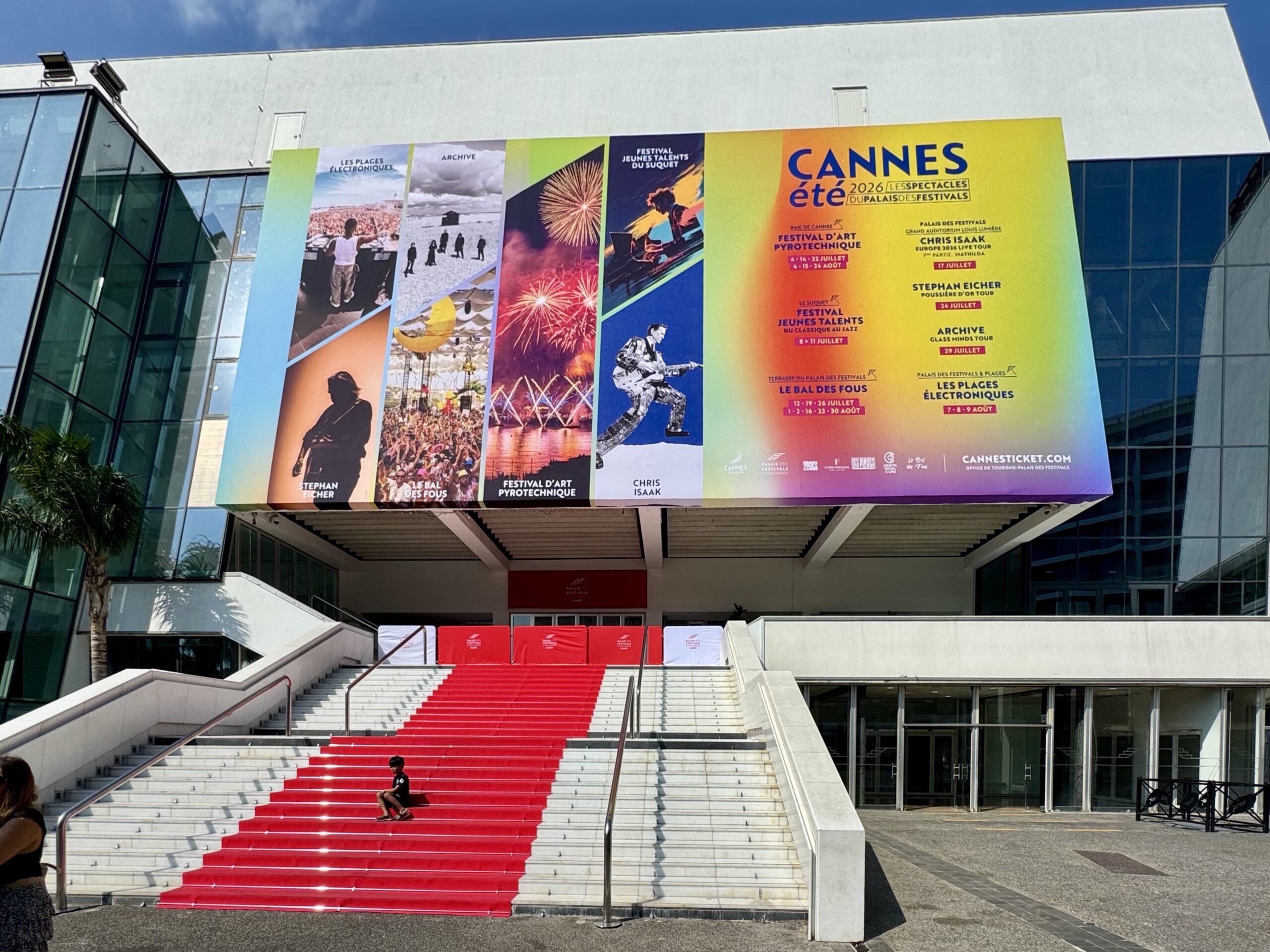Facade of a modern venue with a rainbow-themed festival banner and a red-carpeted staircase leading to the entrance.