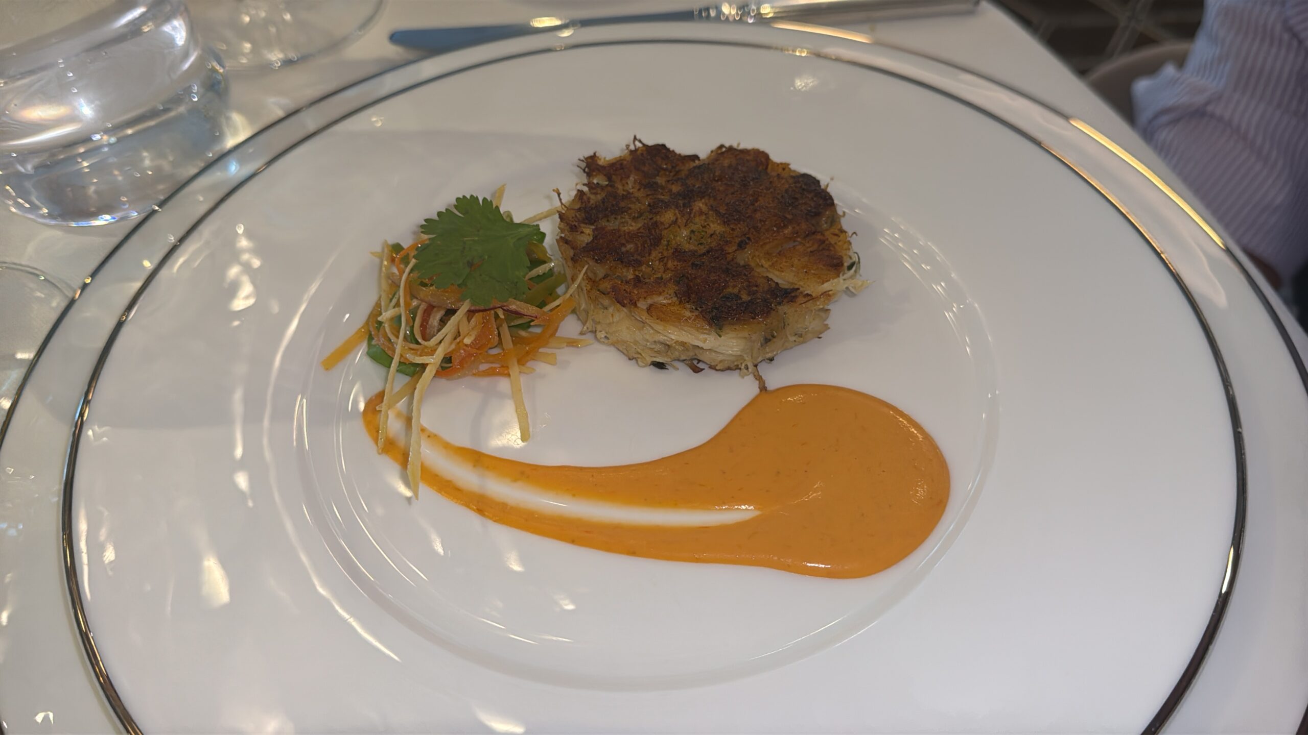 Golden brown, pan-seared patty with a side of julienned carrot and vegetable slaw, garnished with a cilantro leaf, on a white plate with orange sauce swipe