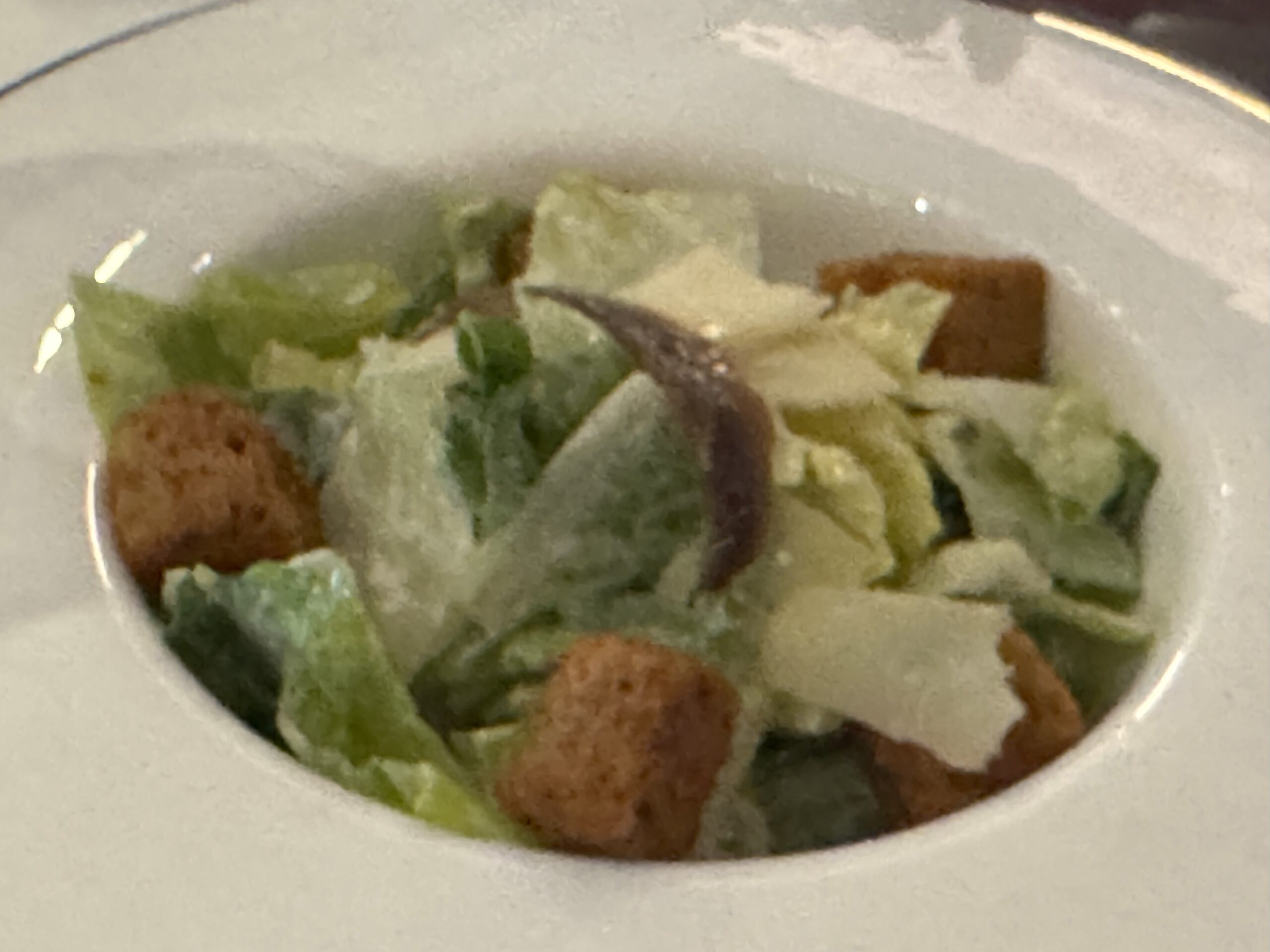 Close-up of a bowl containing mixed green salad with lettuce, cucumber, and croutons in a white dish