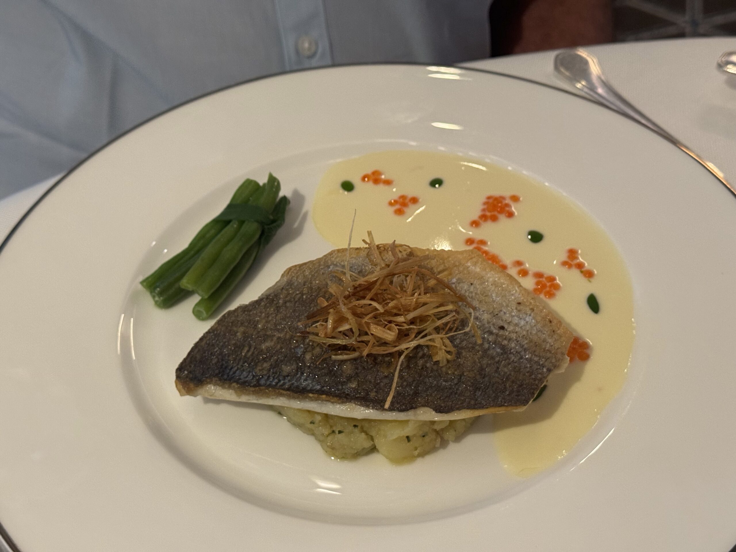 Pan-seared fish fillet with crispy skin over mashed potatoes, green beans, and a light cream sauce with orange roe and green dots on the plate