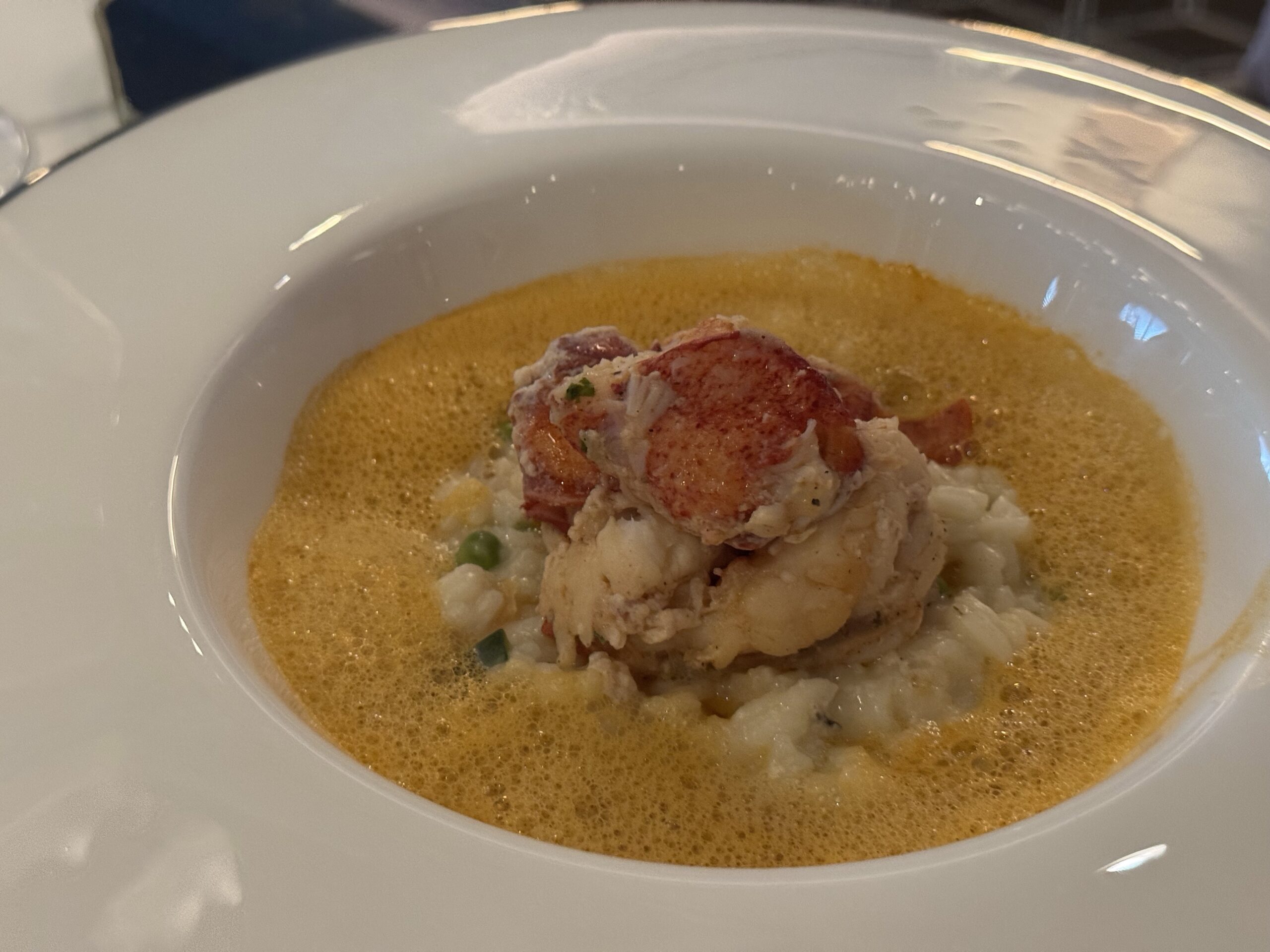 Creamy orange soup in a white bowl topped with lobster meat and green peas.
