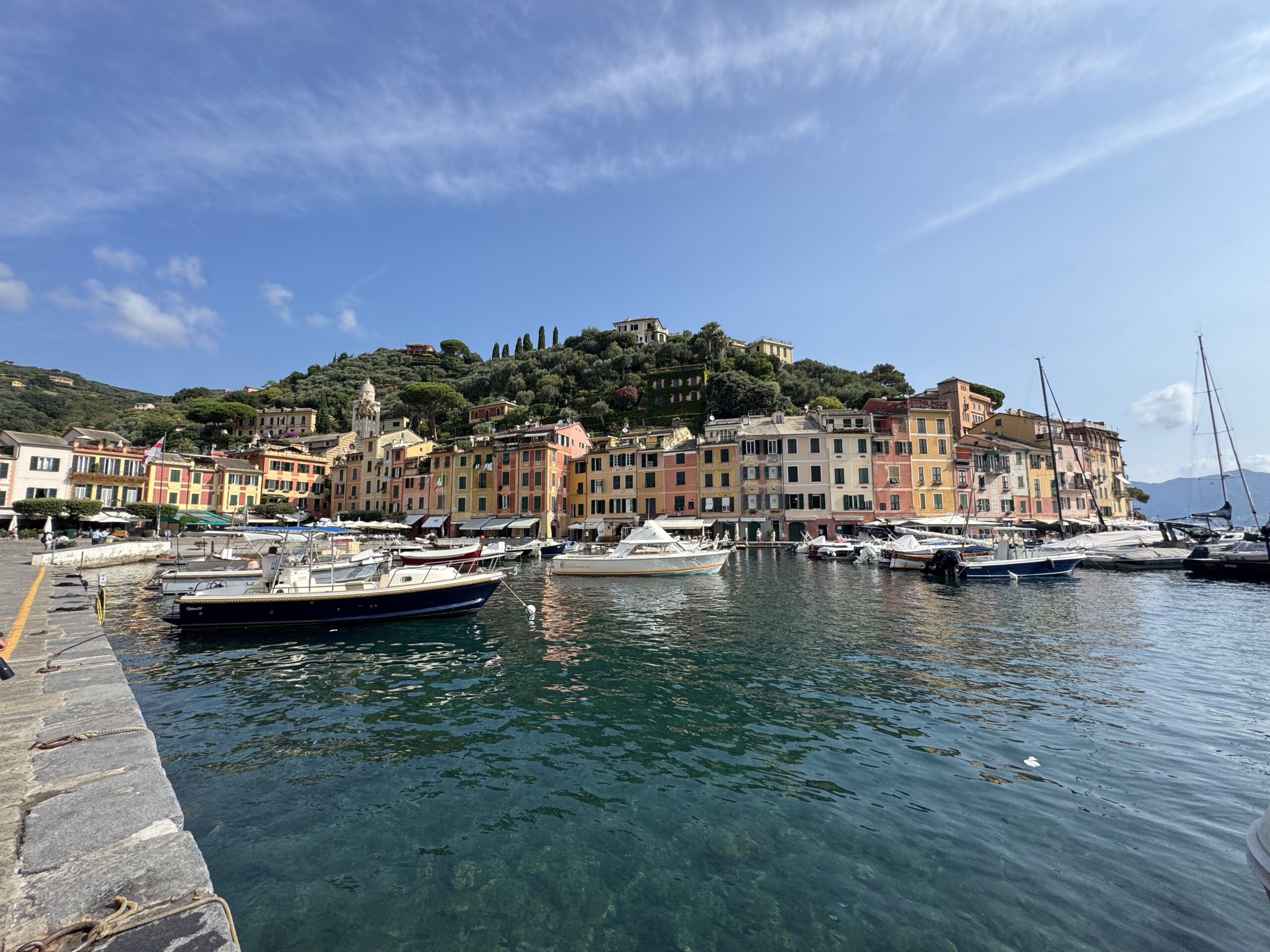 Harbor town with pastel buildings along the water, boats docked in the marina under a clear blue sky.