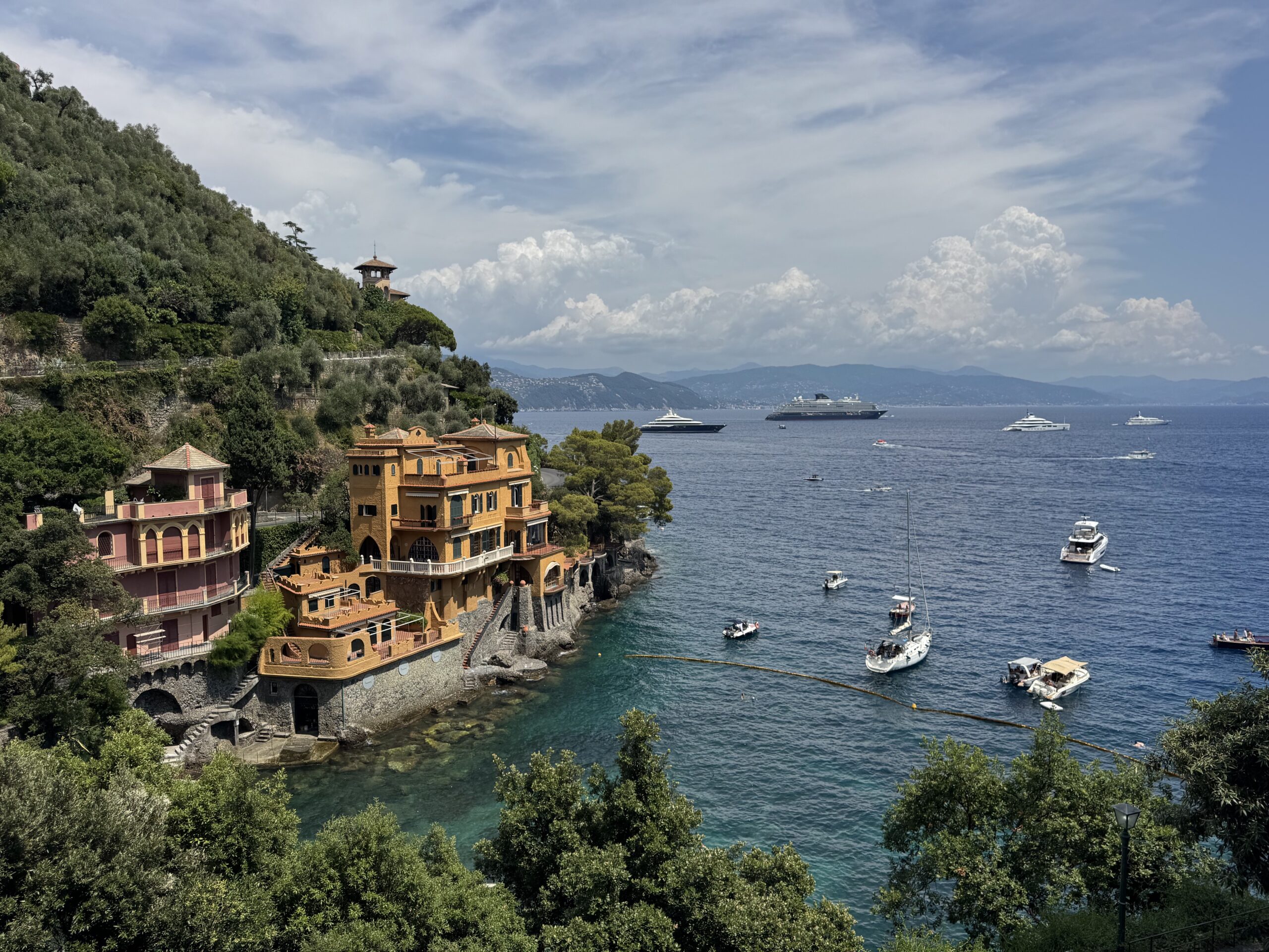 Colorful coastal village built on a rocky hillside beside turquoise water, with boats and yachts in the bay.