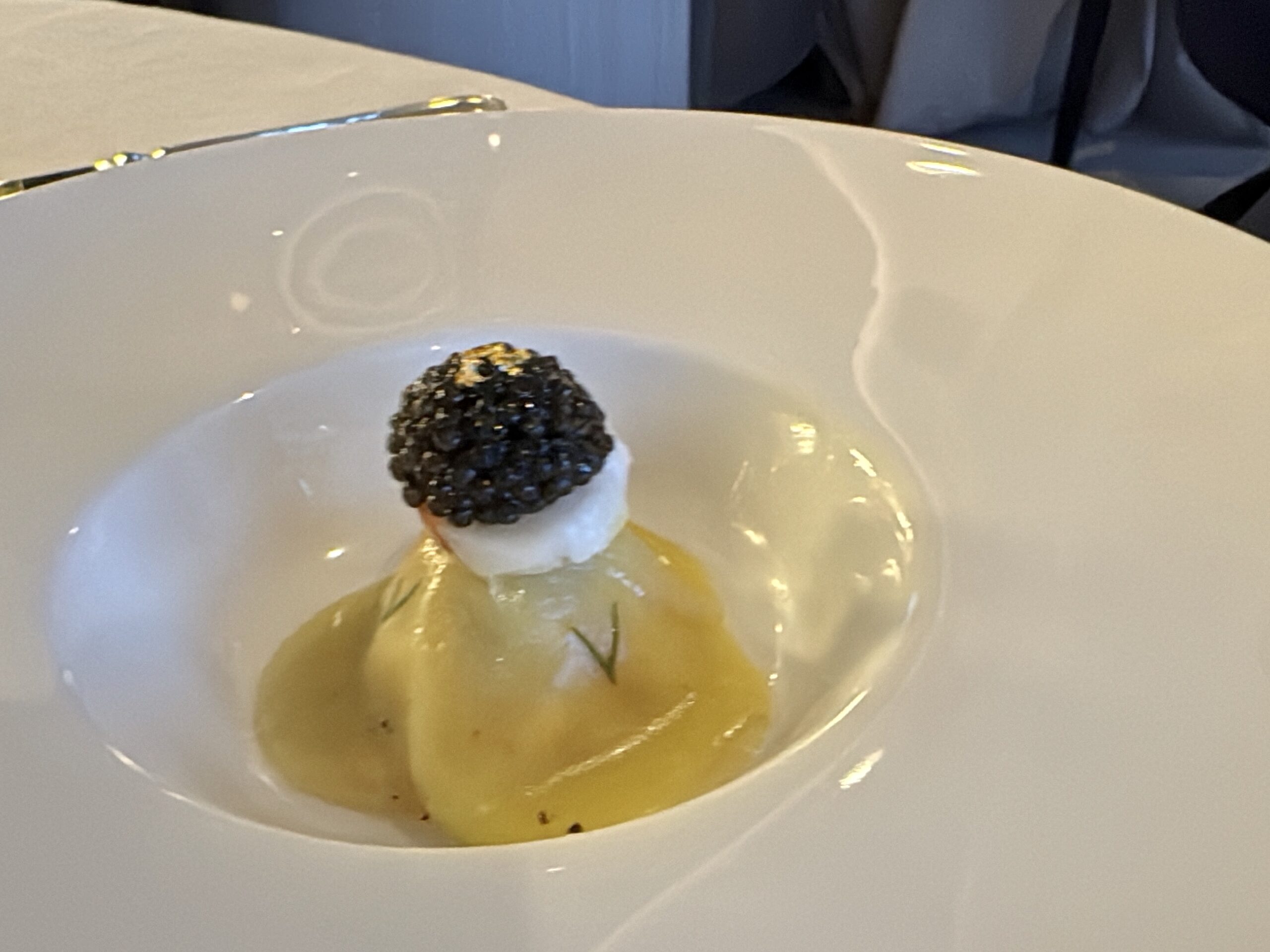 Small plated dessert with a blackberry atop a dollop of cream and citrusy sauce on a white plate