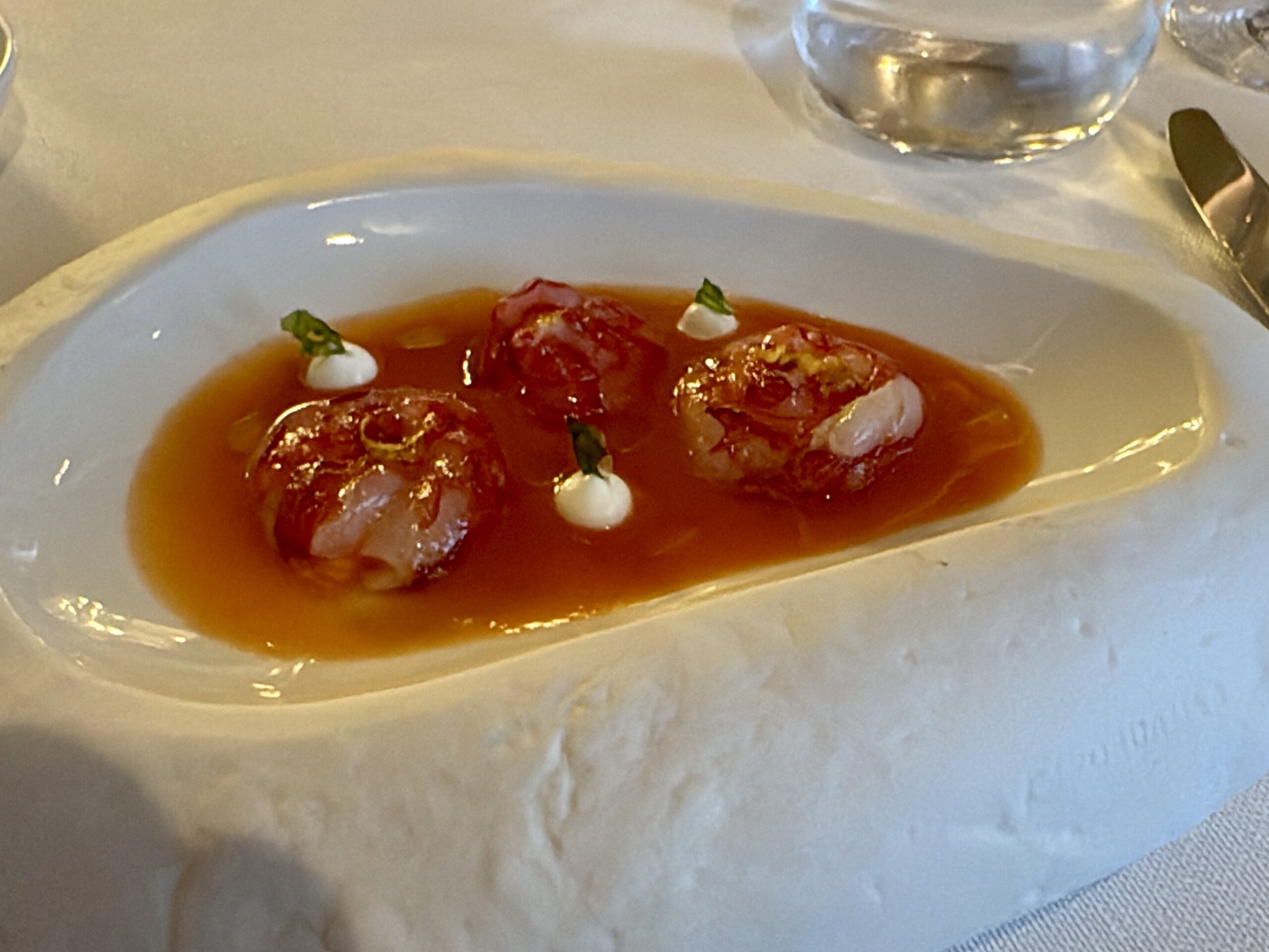 Two meatballs in tomato sauce on a white plate, topped with small dollops of cream and basil leaves.