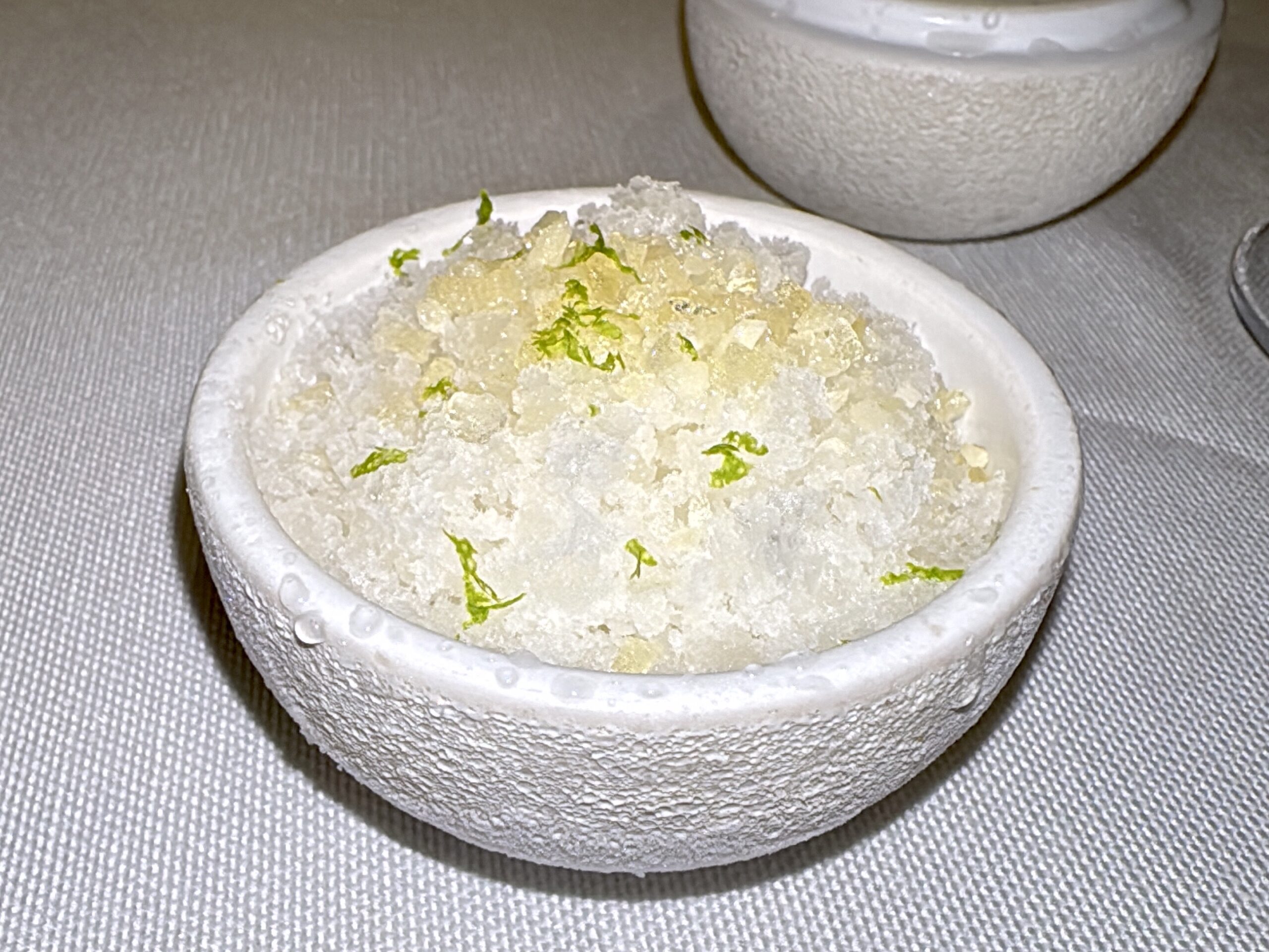 White ceramic bowl filled with coarse salt and lime zest on a textured gray surface.