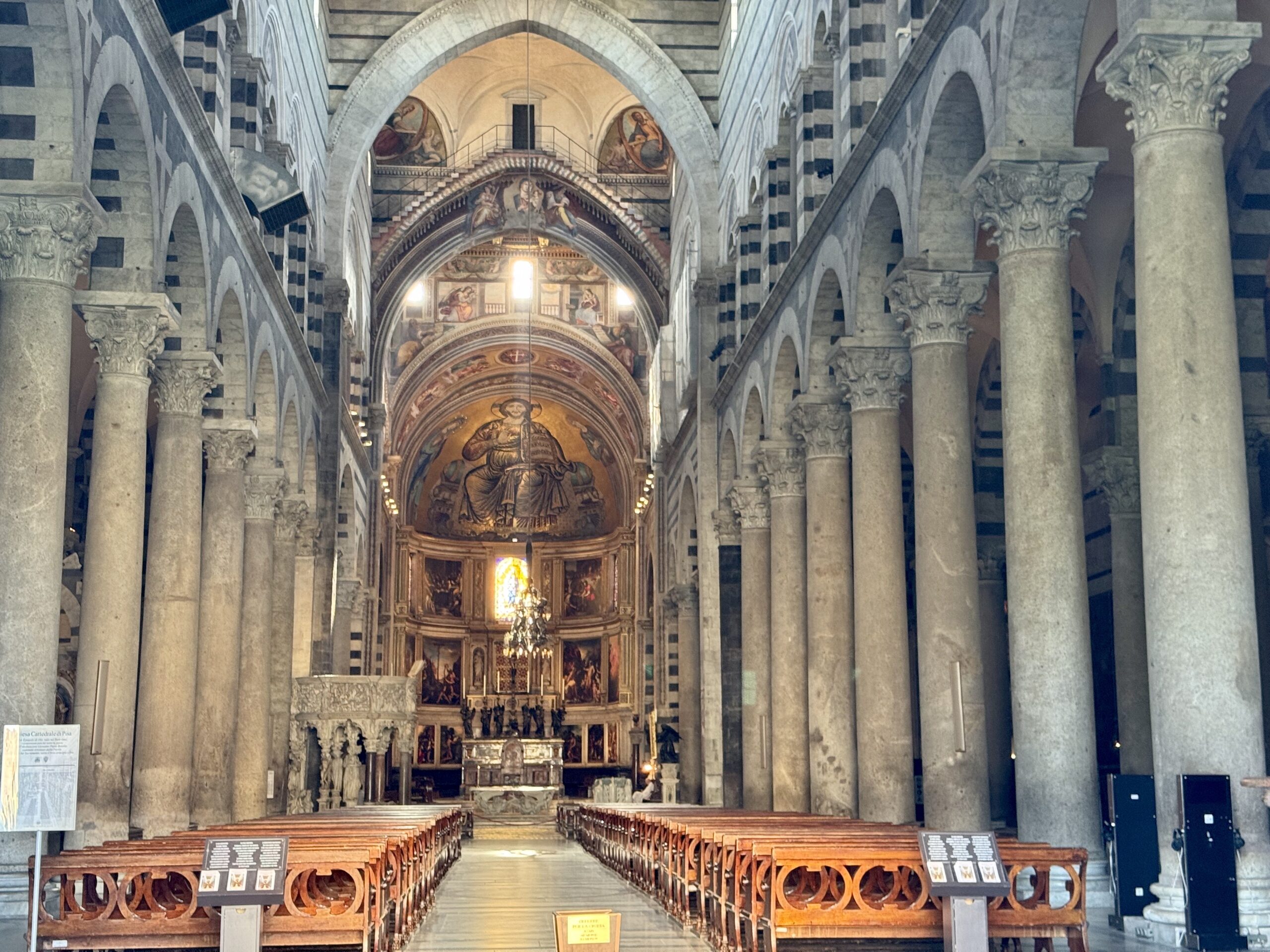Interior of a grand stone cathedral with tall columns and arched vaults leading to an ornate altar and illuminated mosaics.