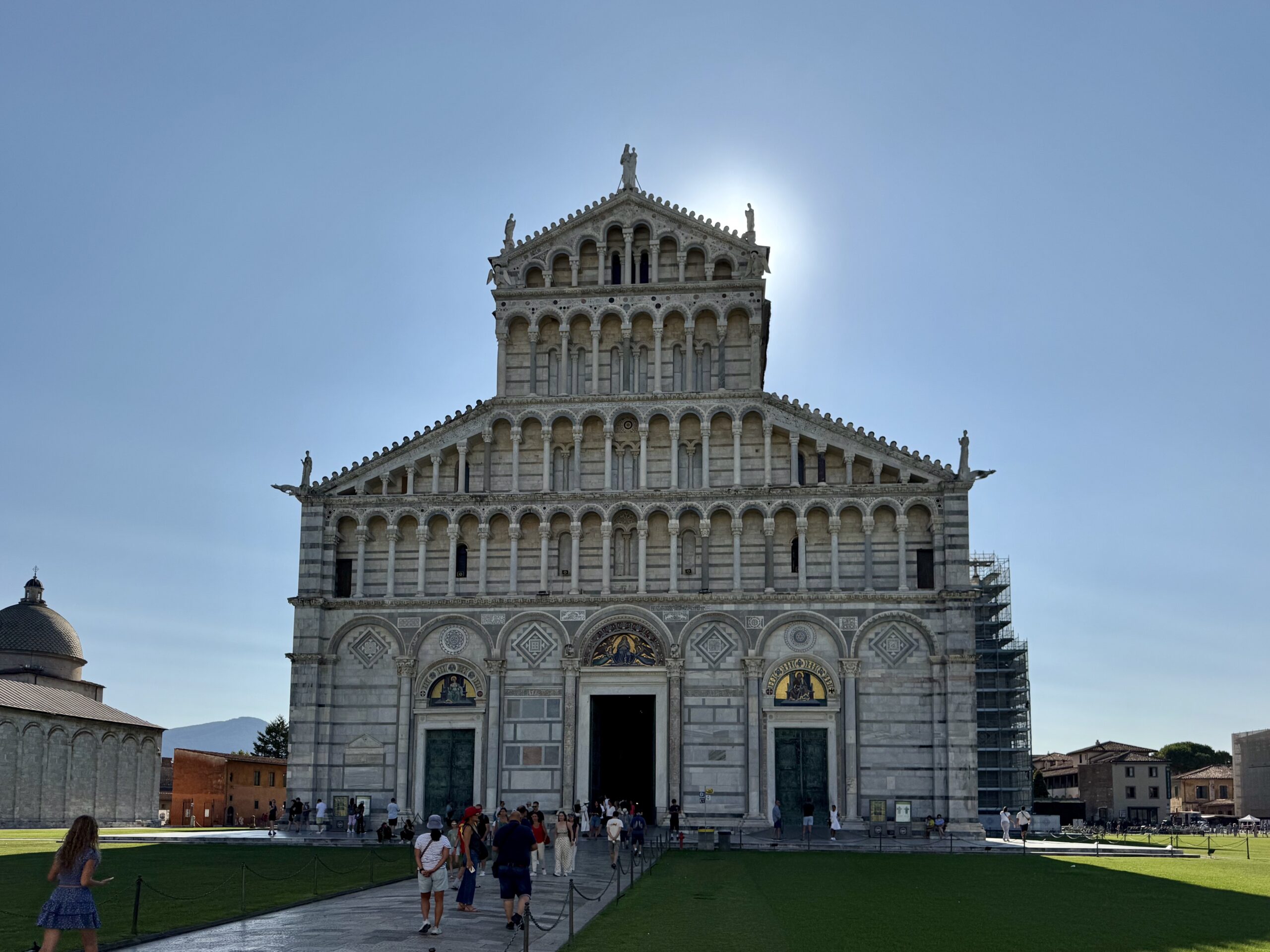 Front façade of a historic cathedral with multiple arches, statues, and a small crowd at the entrance on a clear day.