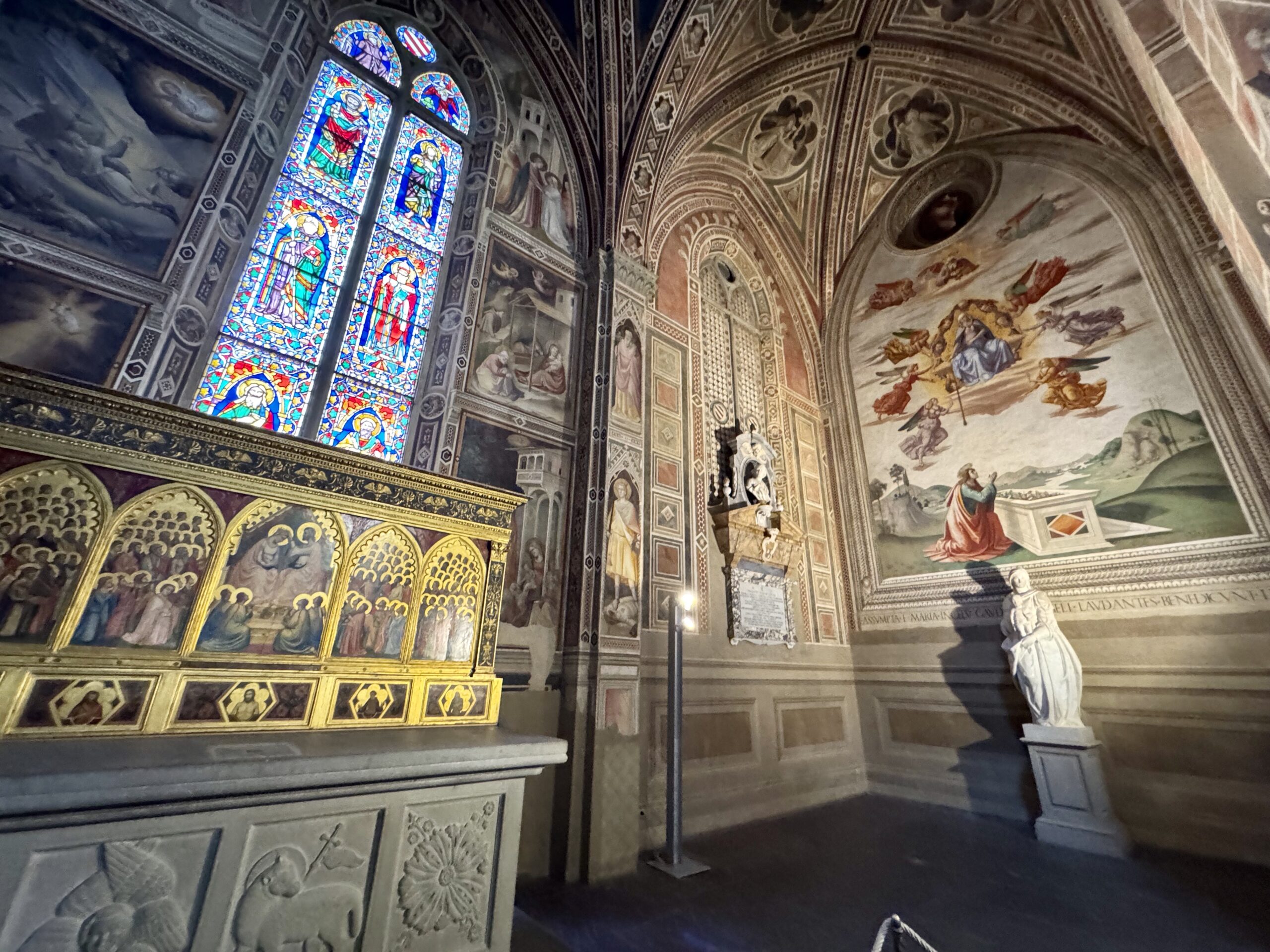Interior of a historic church with colorful stained-glass windows, decorative arches, and a statue in the foreground.