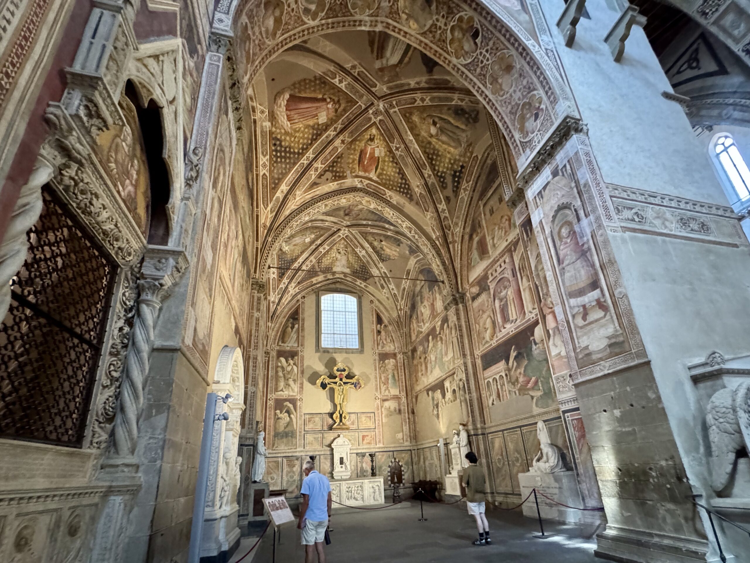 Interior of a richly frescoed church with arched ceilings and ornate stonework, visitors admiring the art.