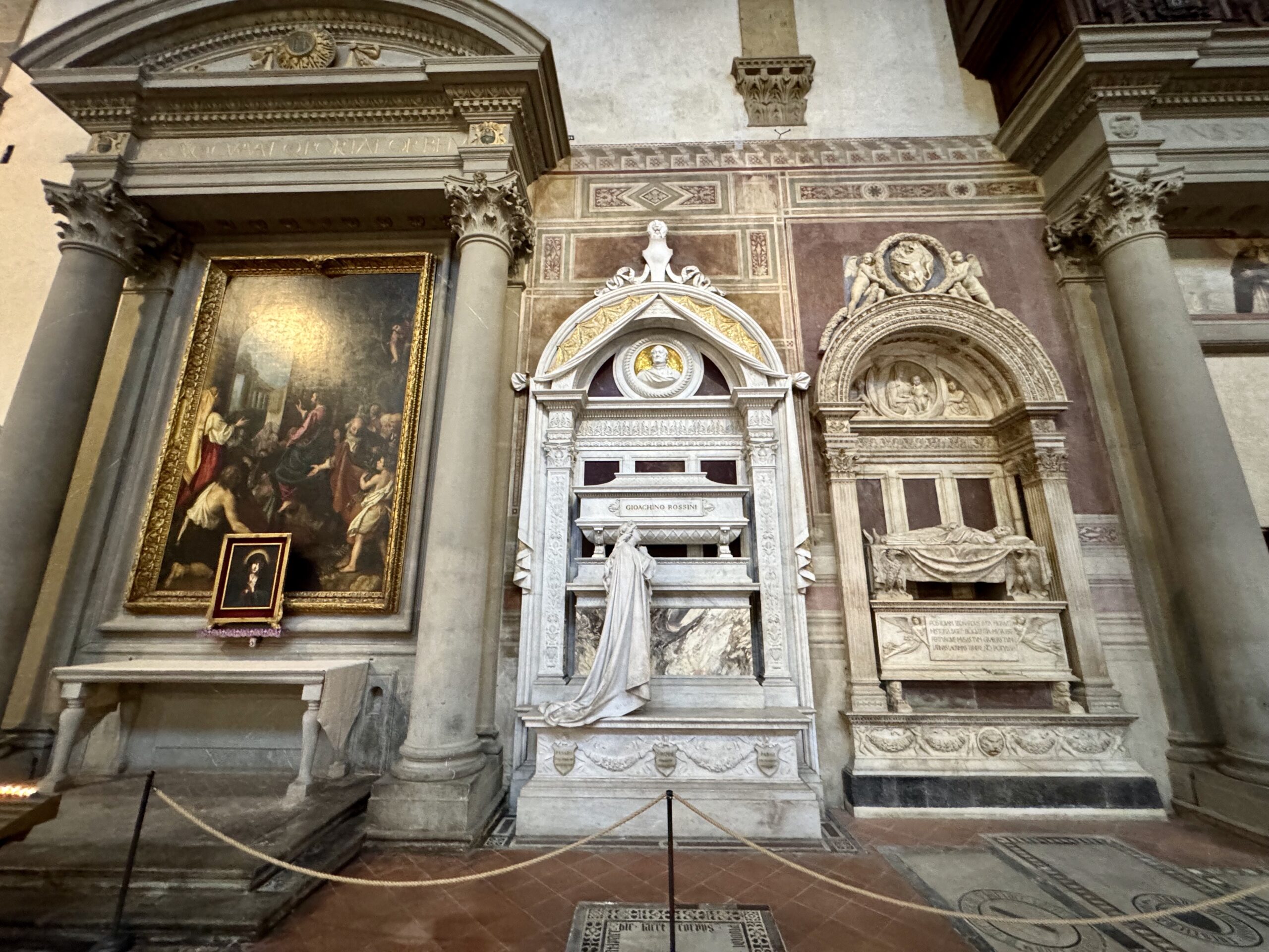 Interior of a historic gallery with marble columns, an ornate frieze, and a large framed painting on the left.