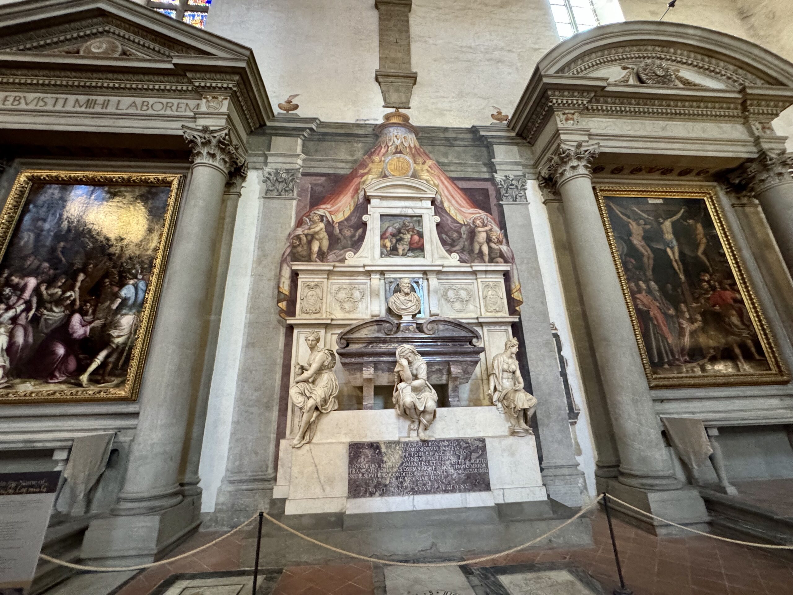 Interior of a grand church with a central ornate altar and stone sculptures, flanked by tall columns and large framed paintings on either side.