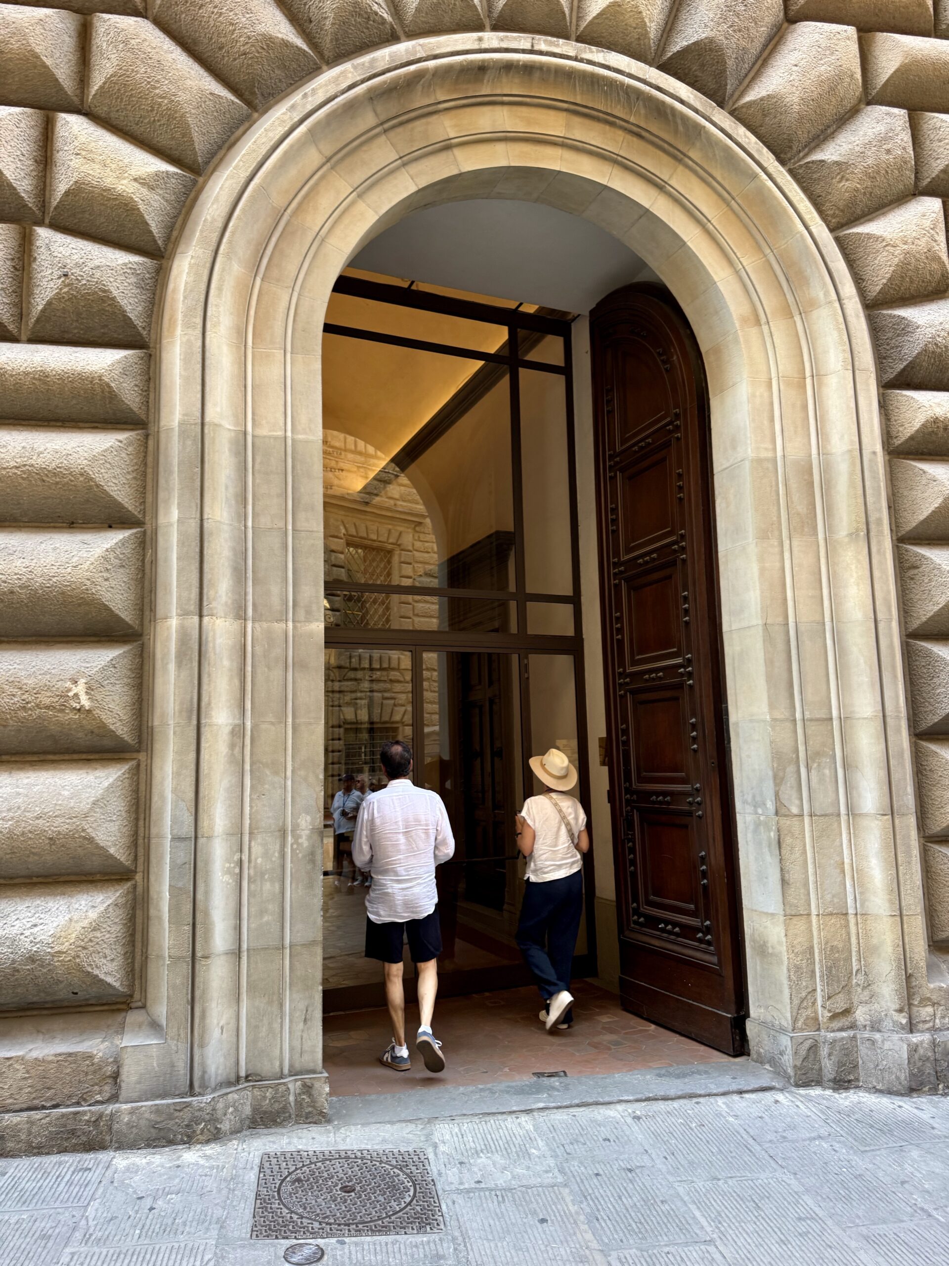 Arched stone doorway with a large wooden door; two people entering a historic-looking building beneath the arch.