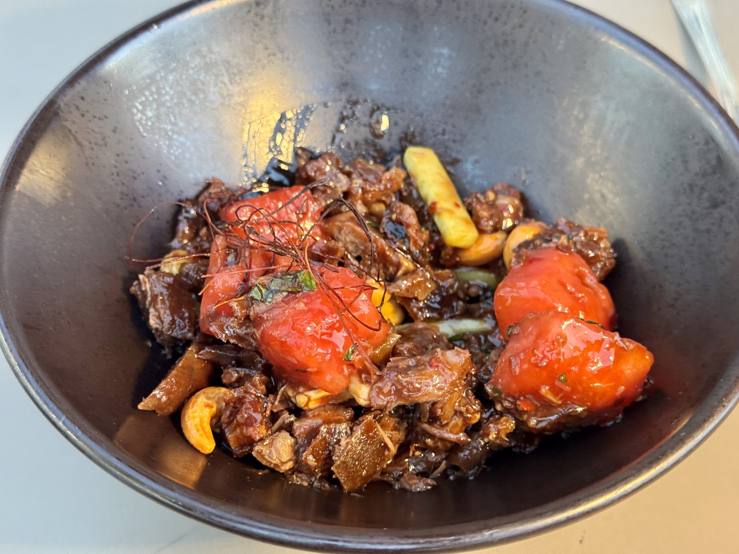 Bowl of braised beef with red peppers and yellow veggies in a dark glossy sauce.
