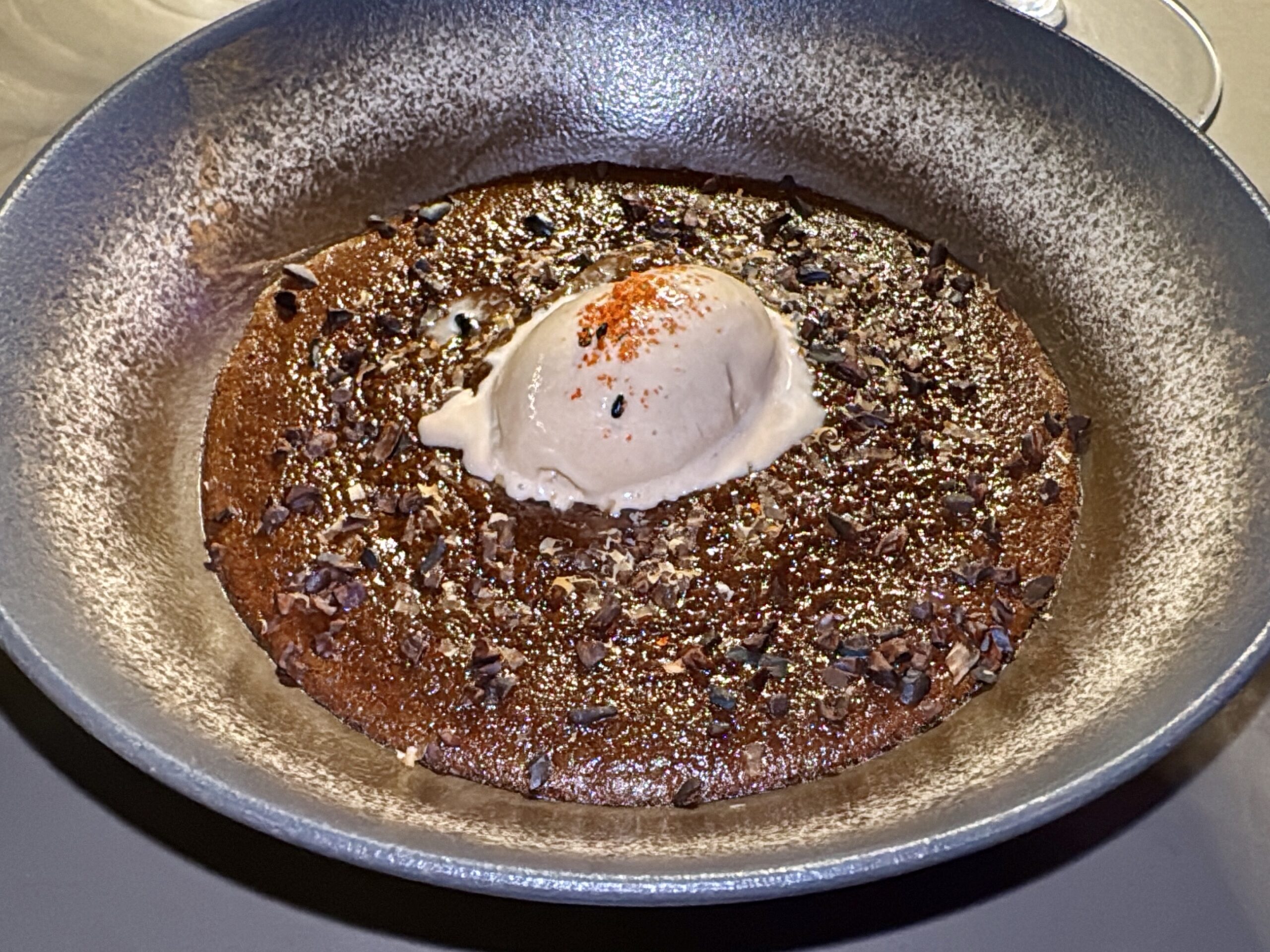 Chocolate lava cake in a round pan topped with a scoop of vanilla ice cream and red sprinkles.