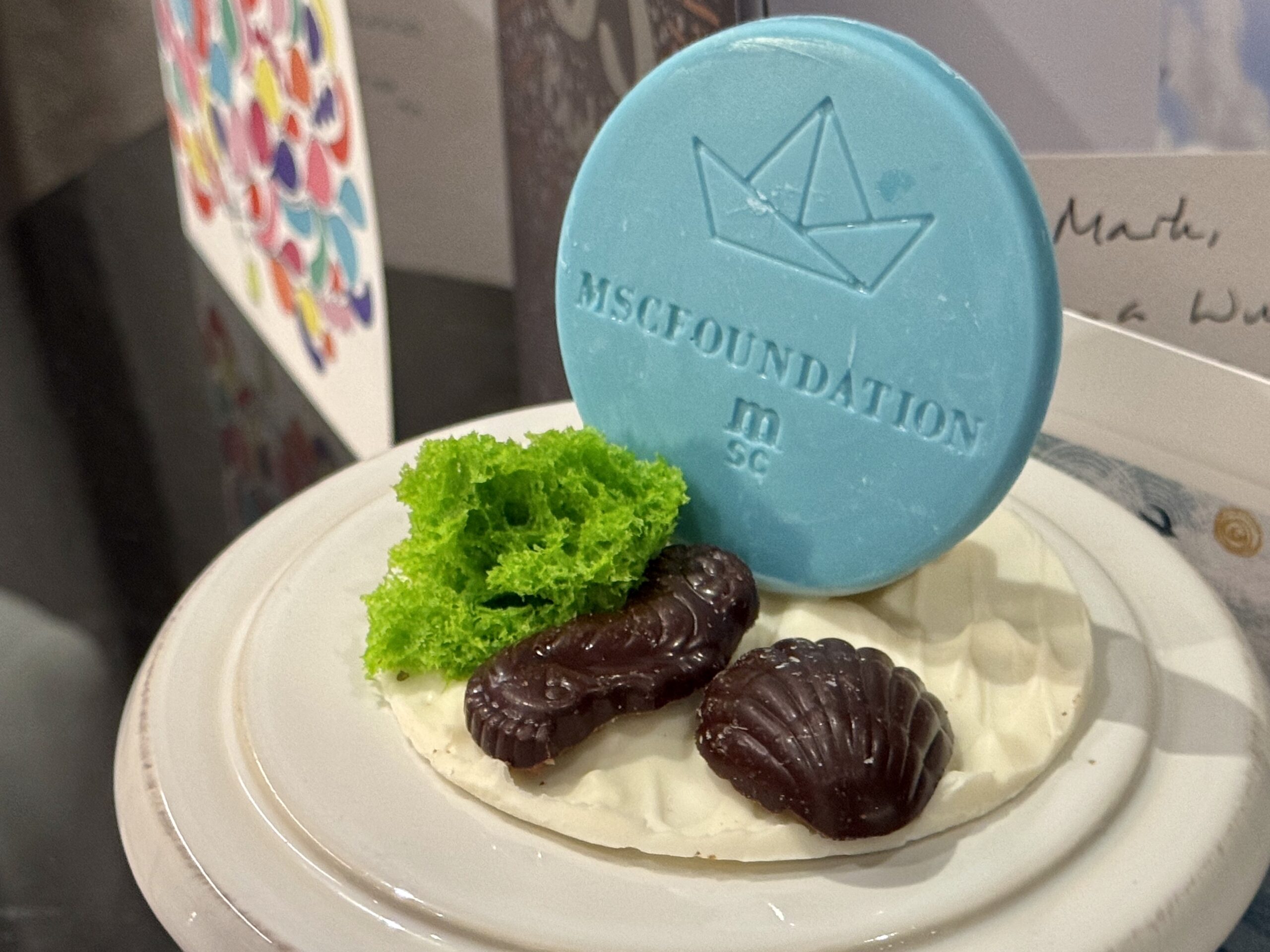 Dessert plate with white frosting, bright green sponge cake, dark chocolate cookies, and a large blue round cookie with a crown design in the background.