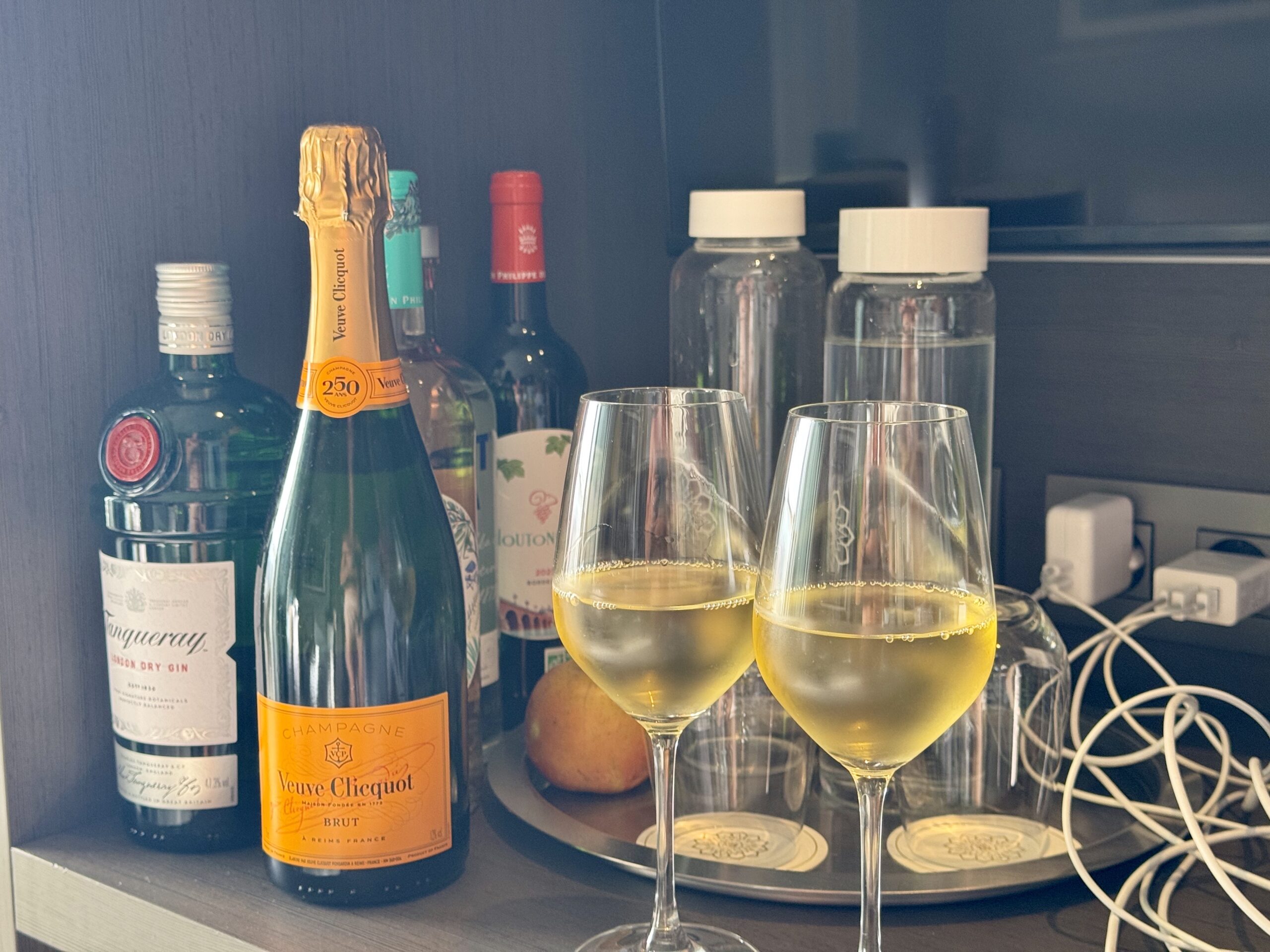 Champagne bottles on a shelf with two filled stemmed glasses in front.