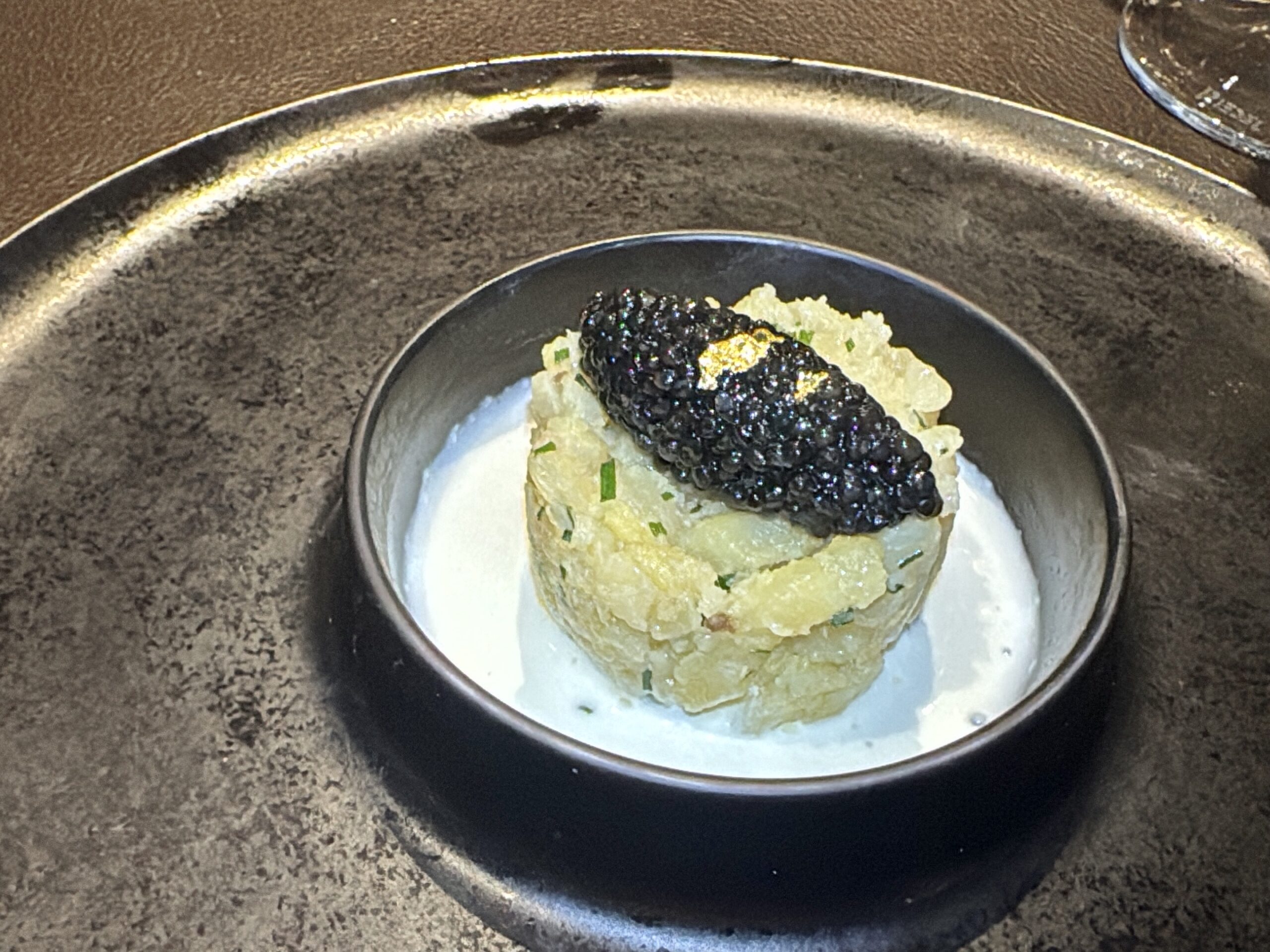 Creamy mashed potatoes in a small metal bowl, topped with black caviar and chopped herbs.
