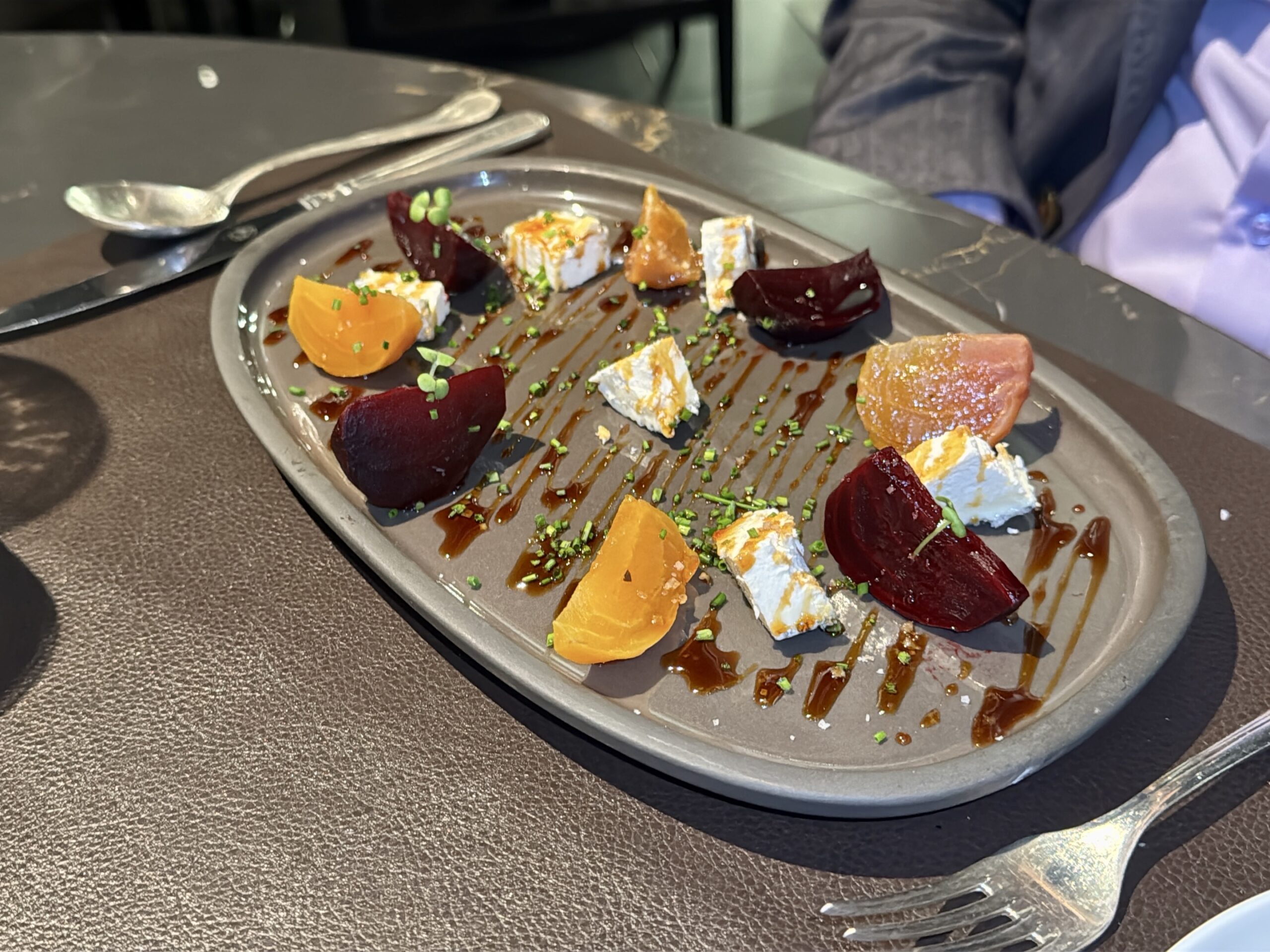 Plate with bite-sized cheese, roasted beet chunks, orange segments, and microgreens drizzled with balsamic glaze on a gray dish.