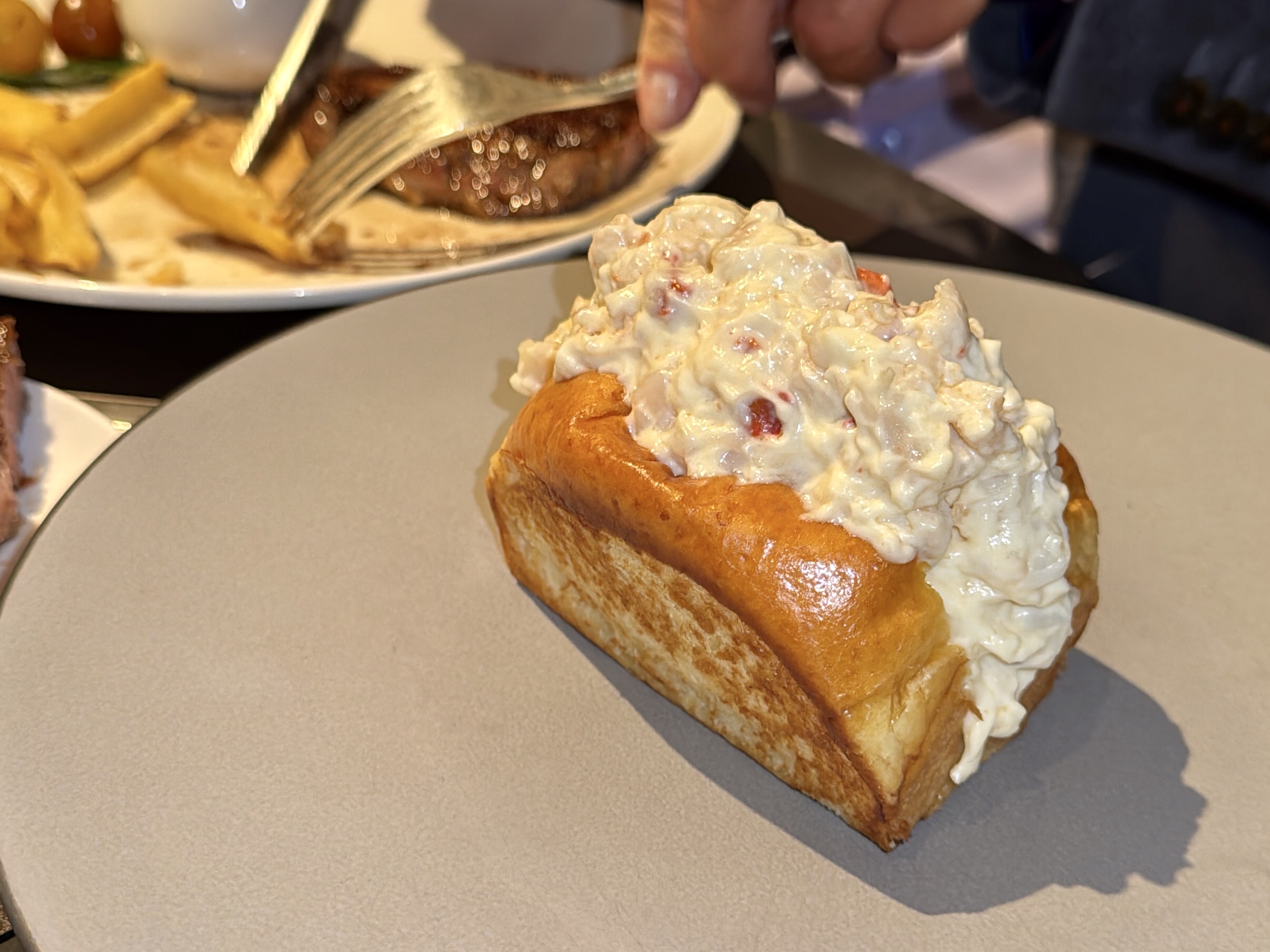 Creamy chicken salad piled on a toasted croissant on a plate, with fries and another plate in the blurred background