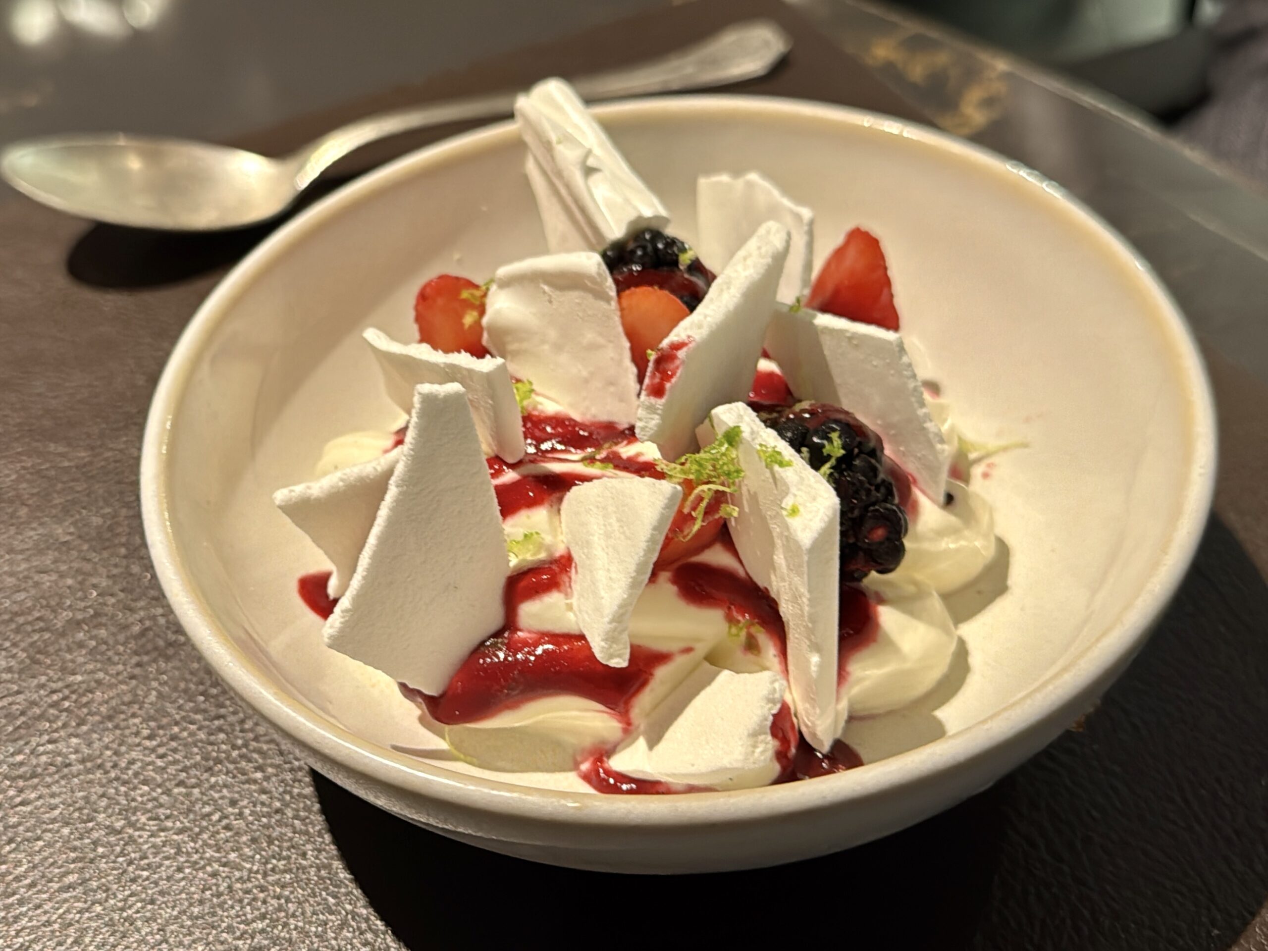 Dessert in a bowl with white meringue shards, whipped cream, red berry sauce, and mixed berries (strawberries and blackberries).