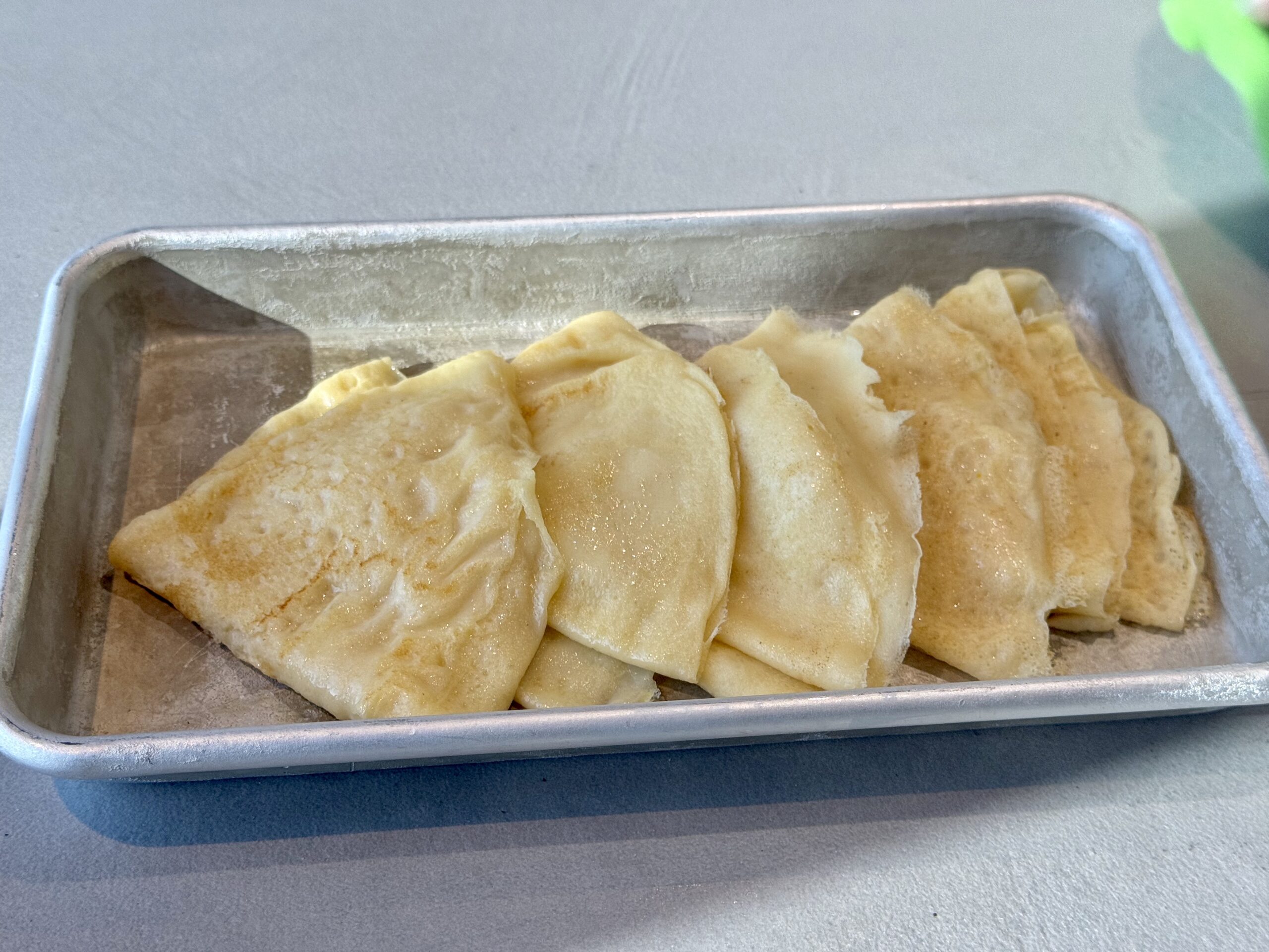 Baking tray filled with folded, pale golden pastries arranged in rows, lightly dusted with flour ices.