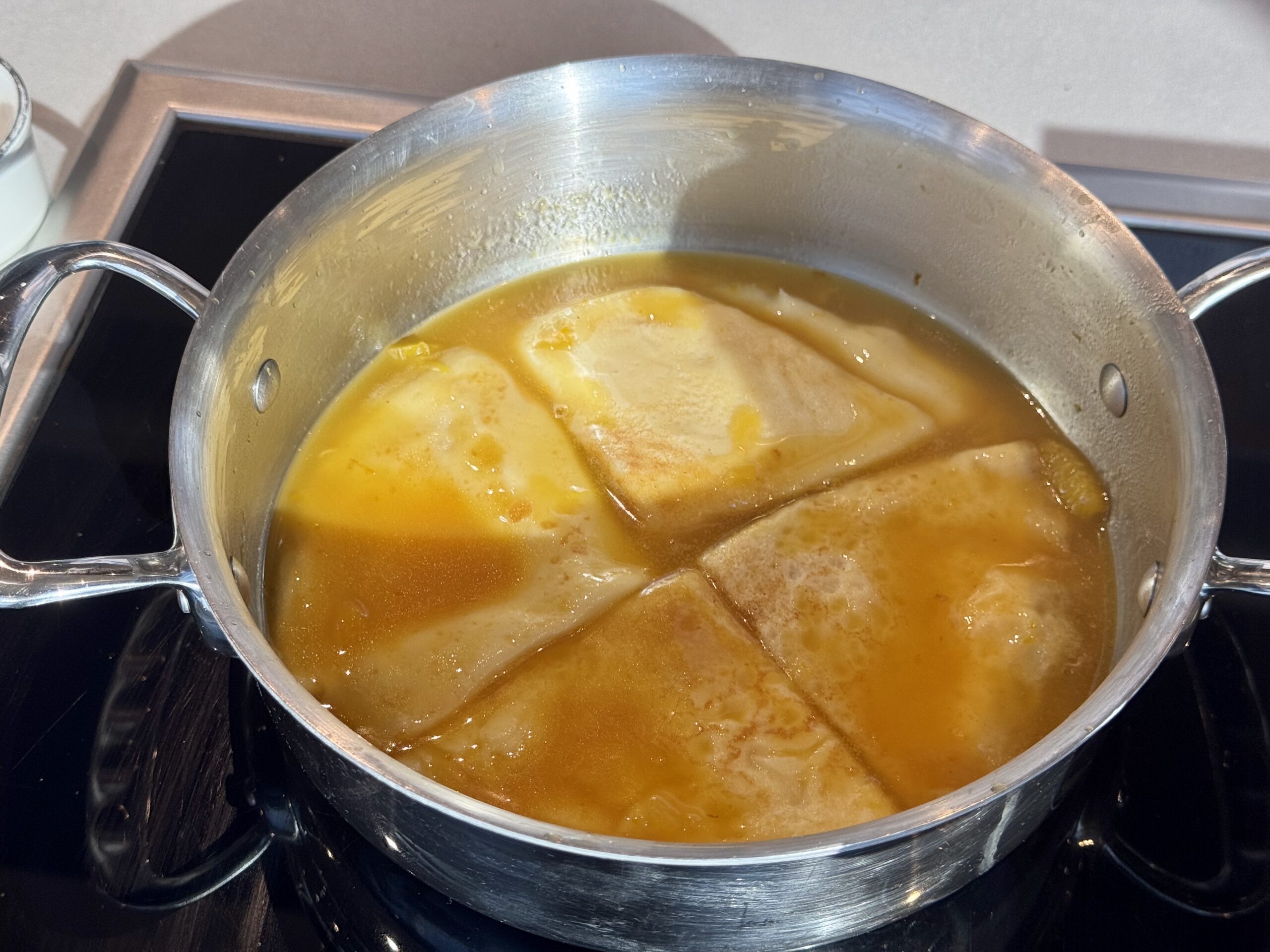 Pot on the stove containing orange broth with pieces of chicken and dumplings.
