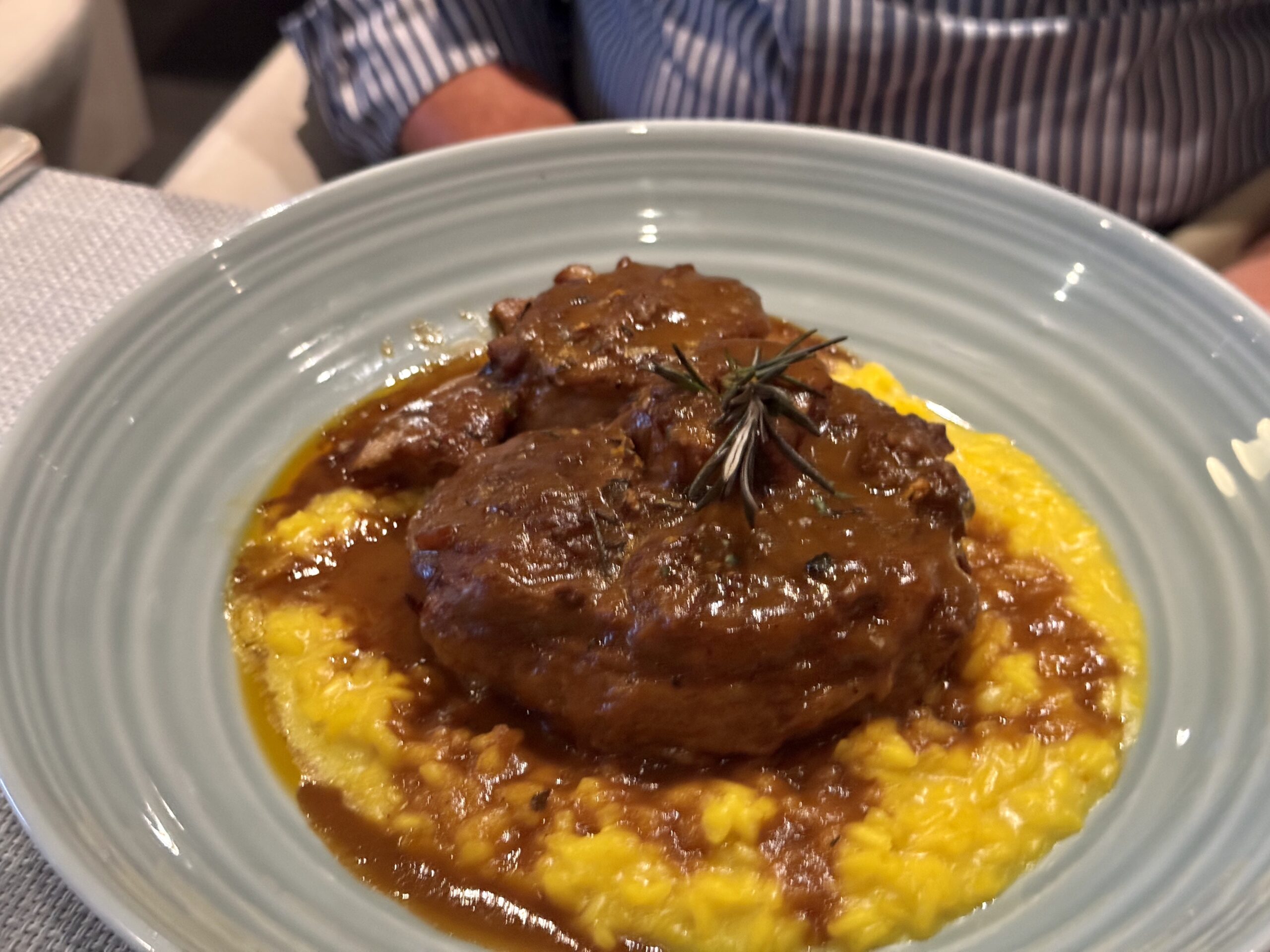Braised beef on a bed of yellow polenta with a rosemary garnish, served on a blue plate.