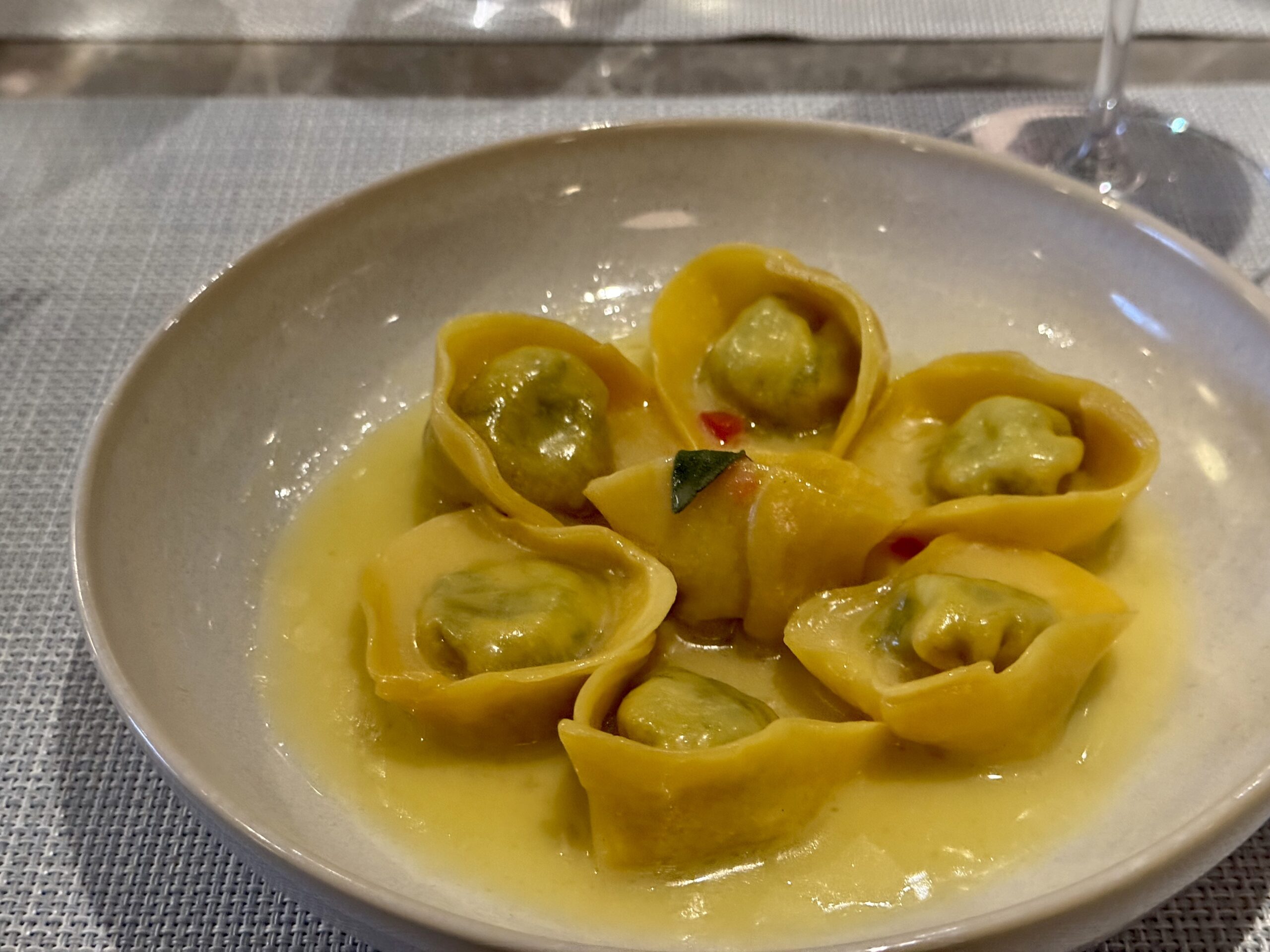 Yellow tortellini pasta with green filling in a pale sauce on a white plate.